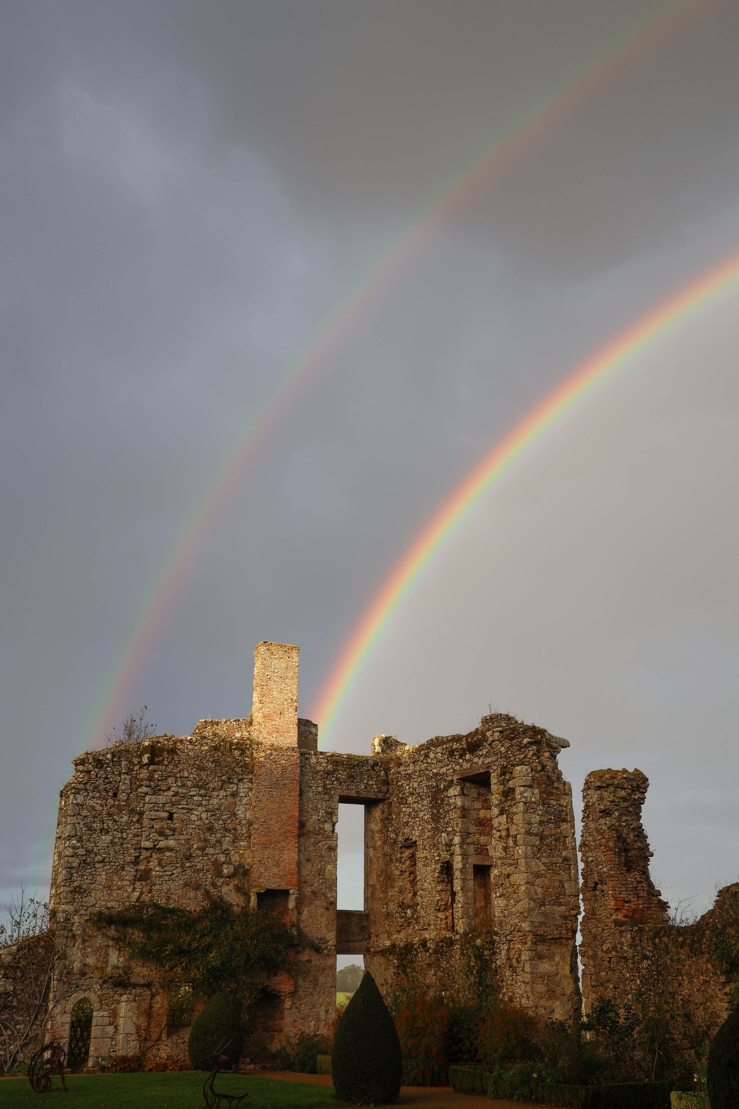 Double rainbow arching over ancient stone castle ruins under dramatic stormy sky.