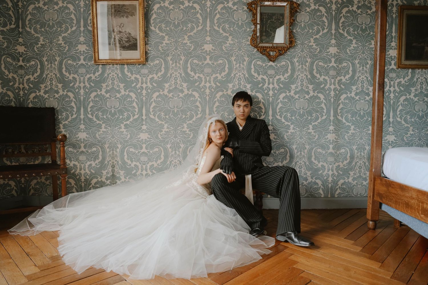 Bride and groom sit together on the floor of a vintage chateau room with ornate damask wallpaper.