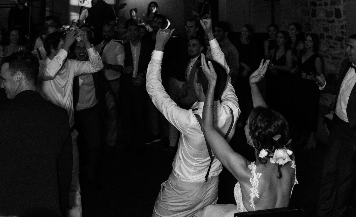 Black and white photo of wedding guests dancing and celebrating joyfully at a lively wedding reception.
