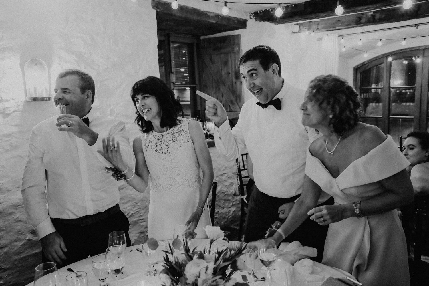 Wedding guests laugh and celebrate together during a joyful toast at a rustic wedding reception dinner.