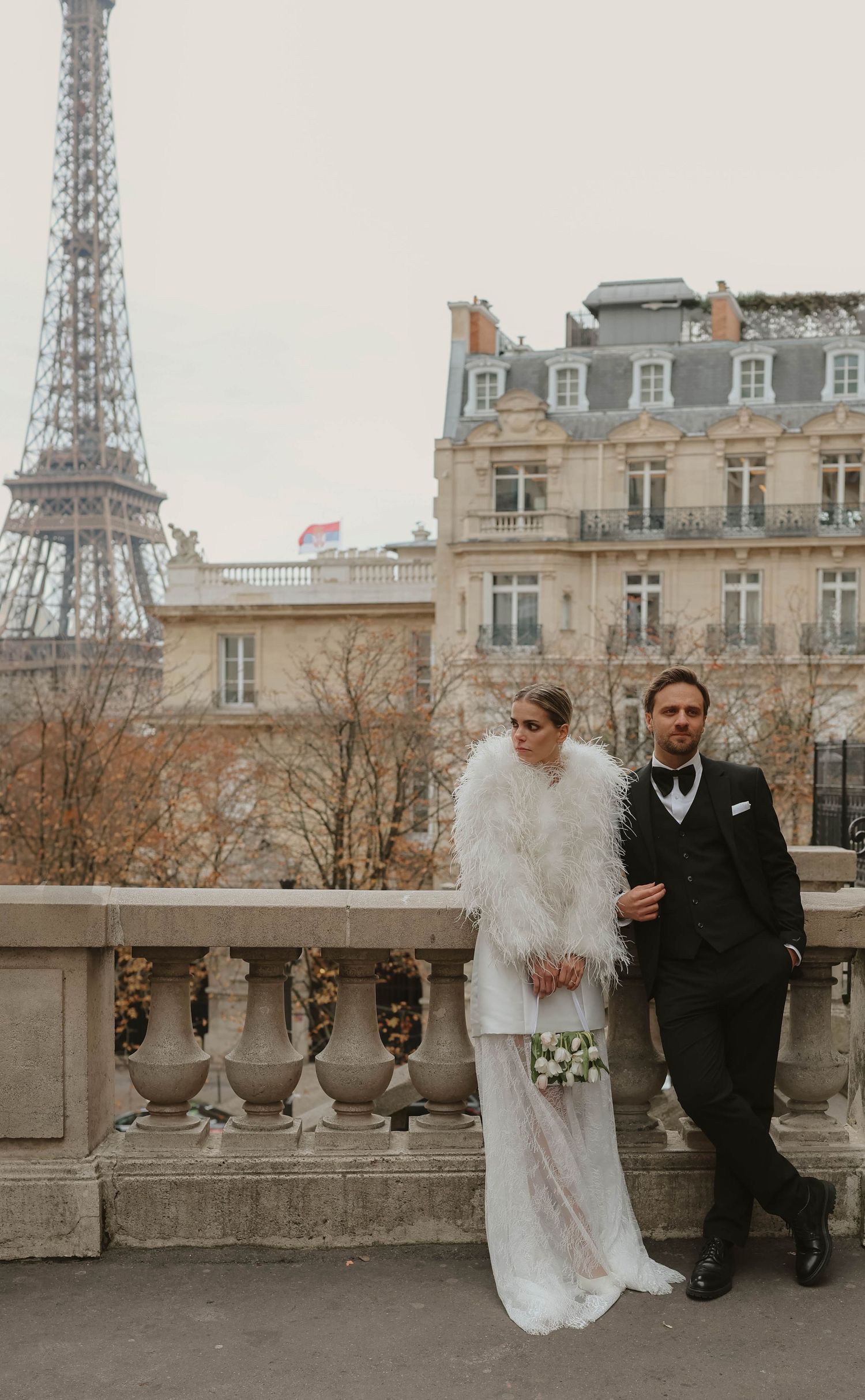 Bride in feather wrap and groom in tuxedo posing with the Eiffel Tower in Paris.