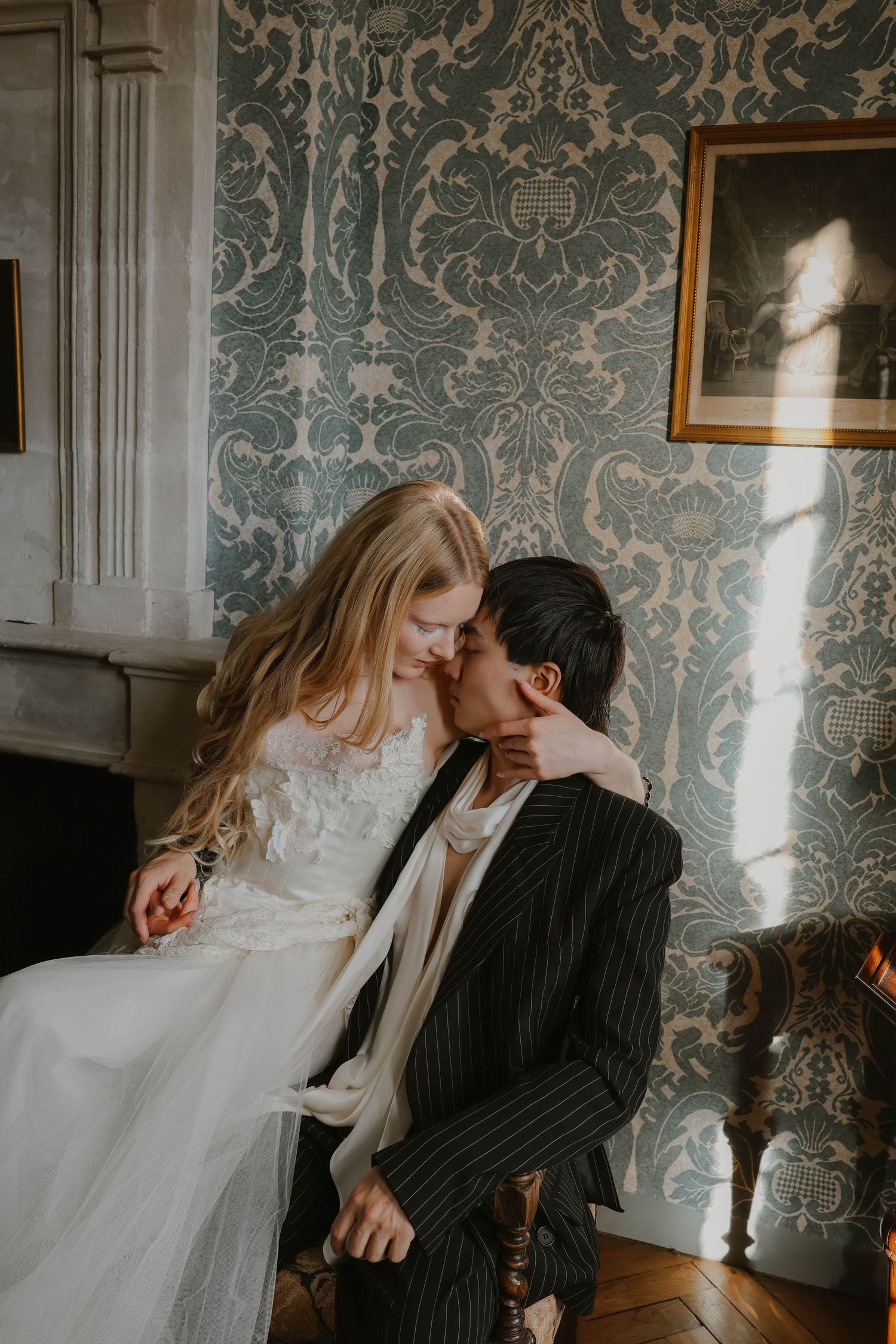 Romantic couple in wedding attire sharing an intimate moment against ornate wallpaper.