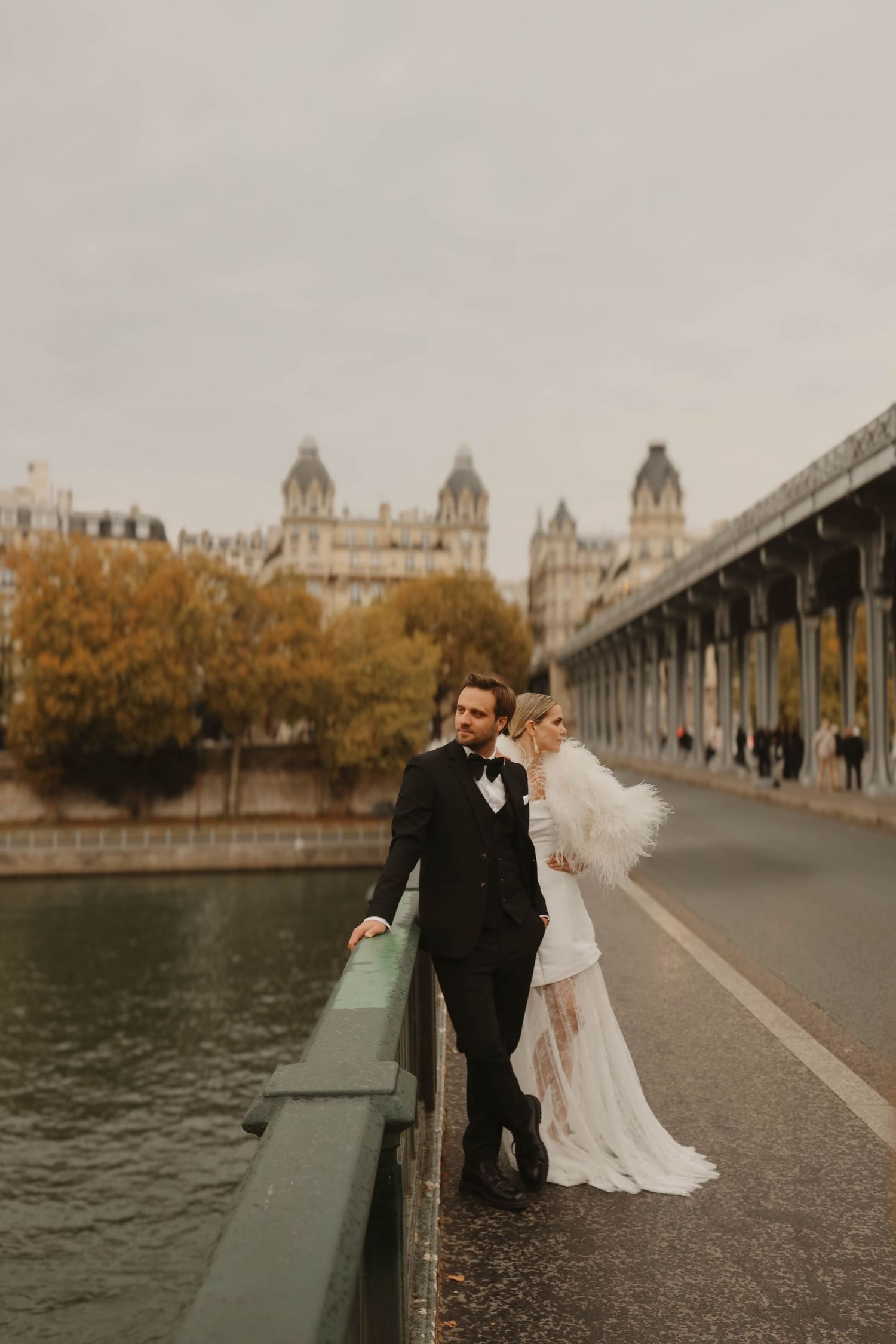 Elegant bride and groom posing on a Parisian bridge over the Seine River with historic architecture in the background.