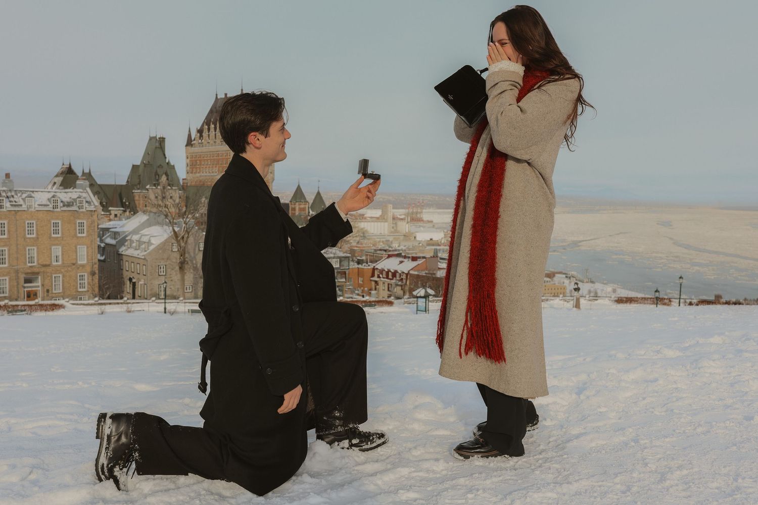 Man proposes on one knee in snowy winter landscape with historic castle backdrop.