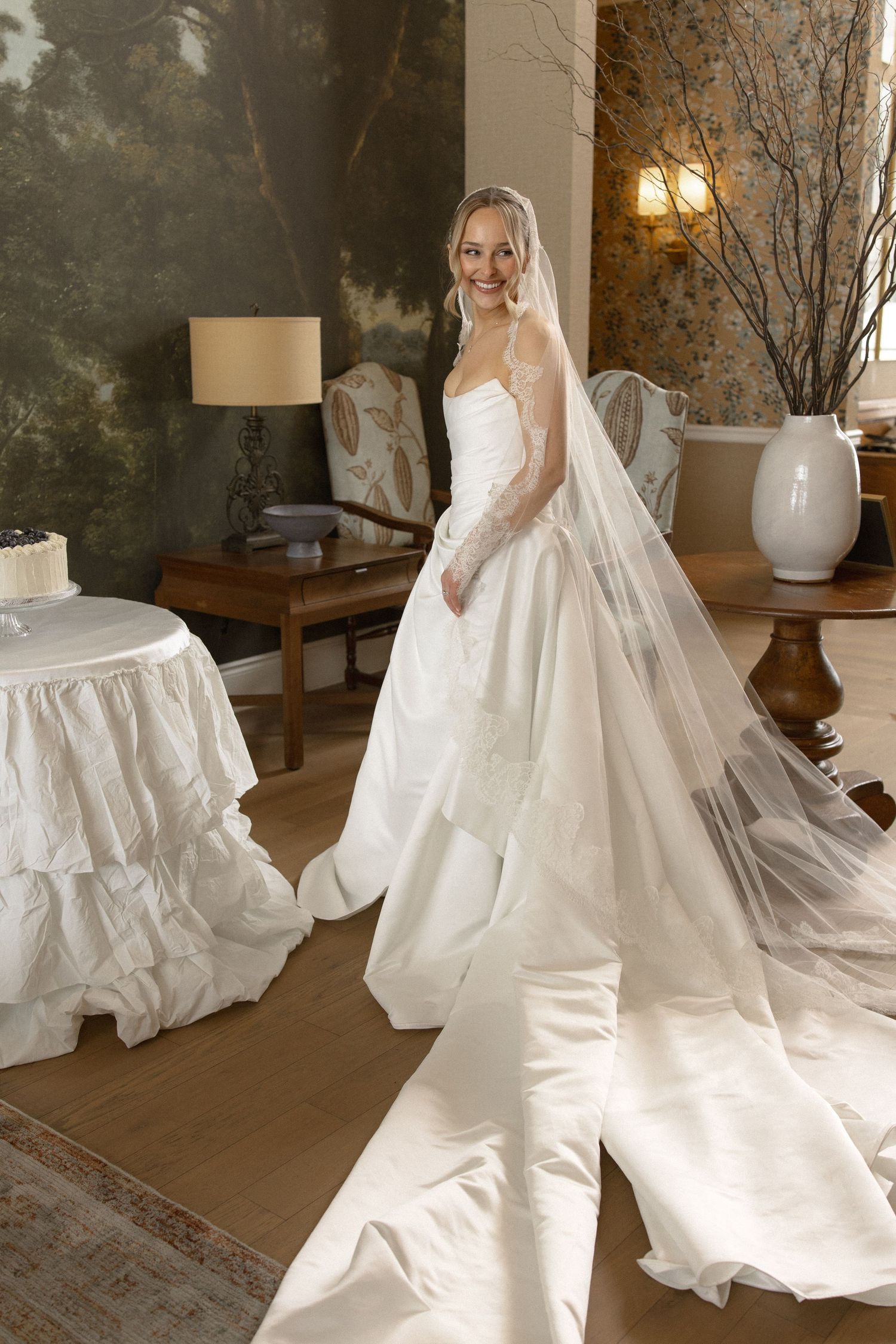 Radiant bride in strapless ball gown with long cathedral veil and lace gloves smiling joyfully.