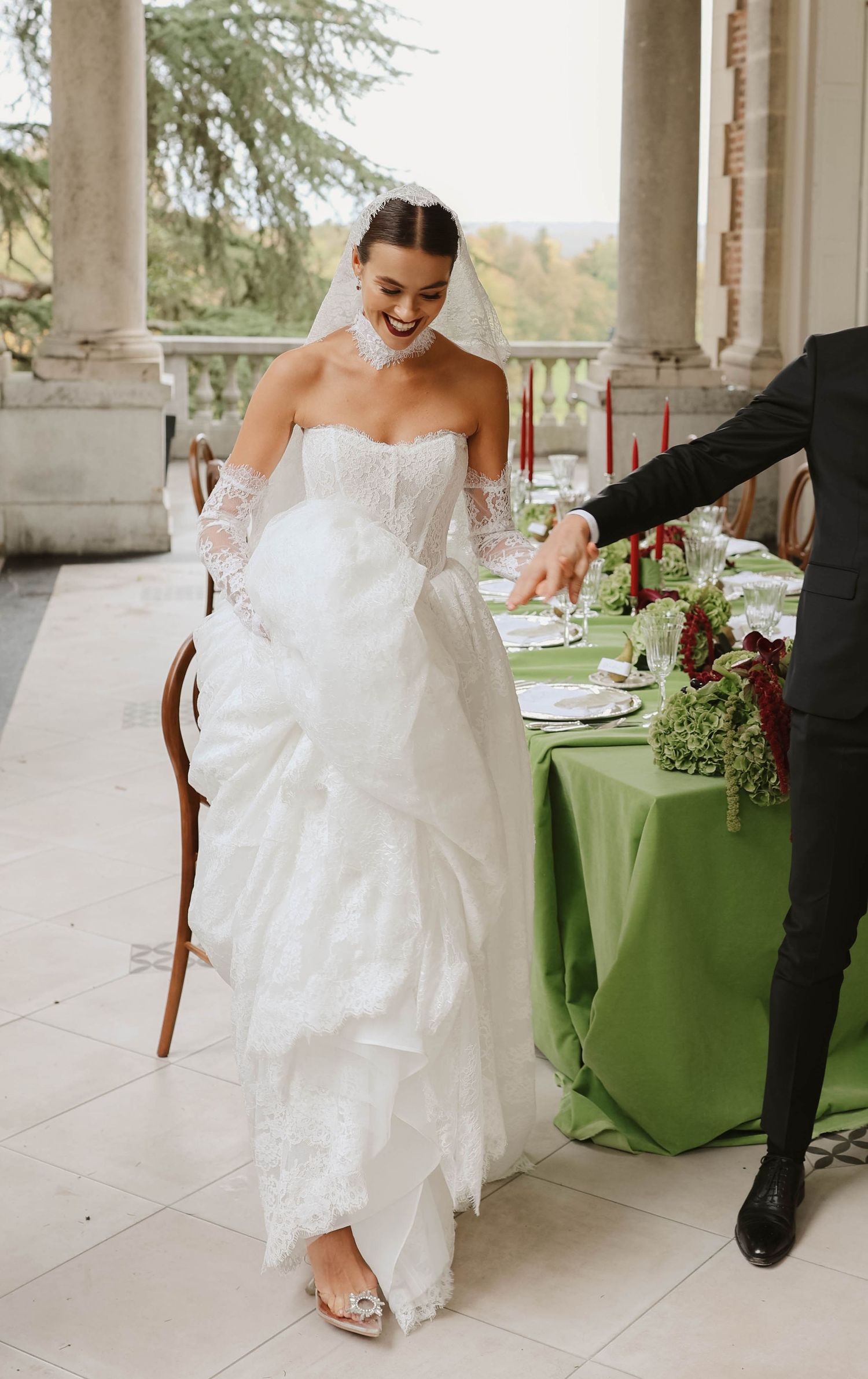 Radiant bride in strapless lace wedding gown laughing beside an elegantly decorated green wedding reception table.