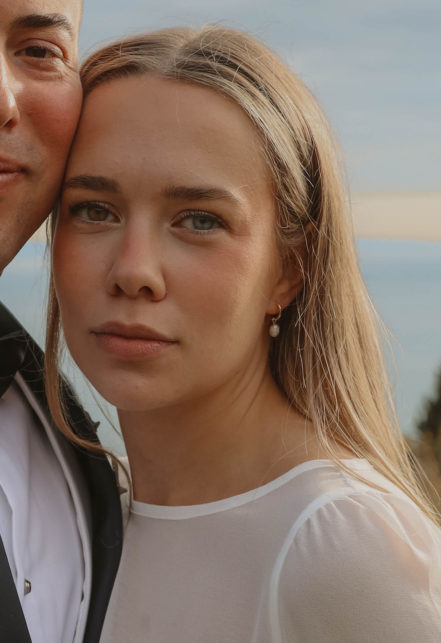 Close-up portrait of blonde bride with pearl earrings looking at camera on wedding day.