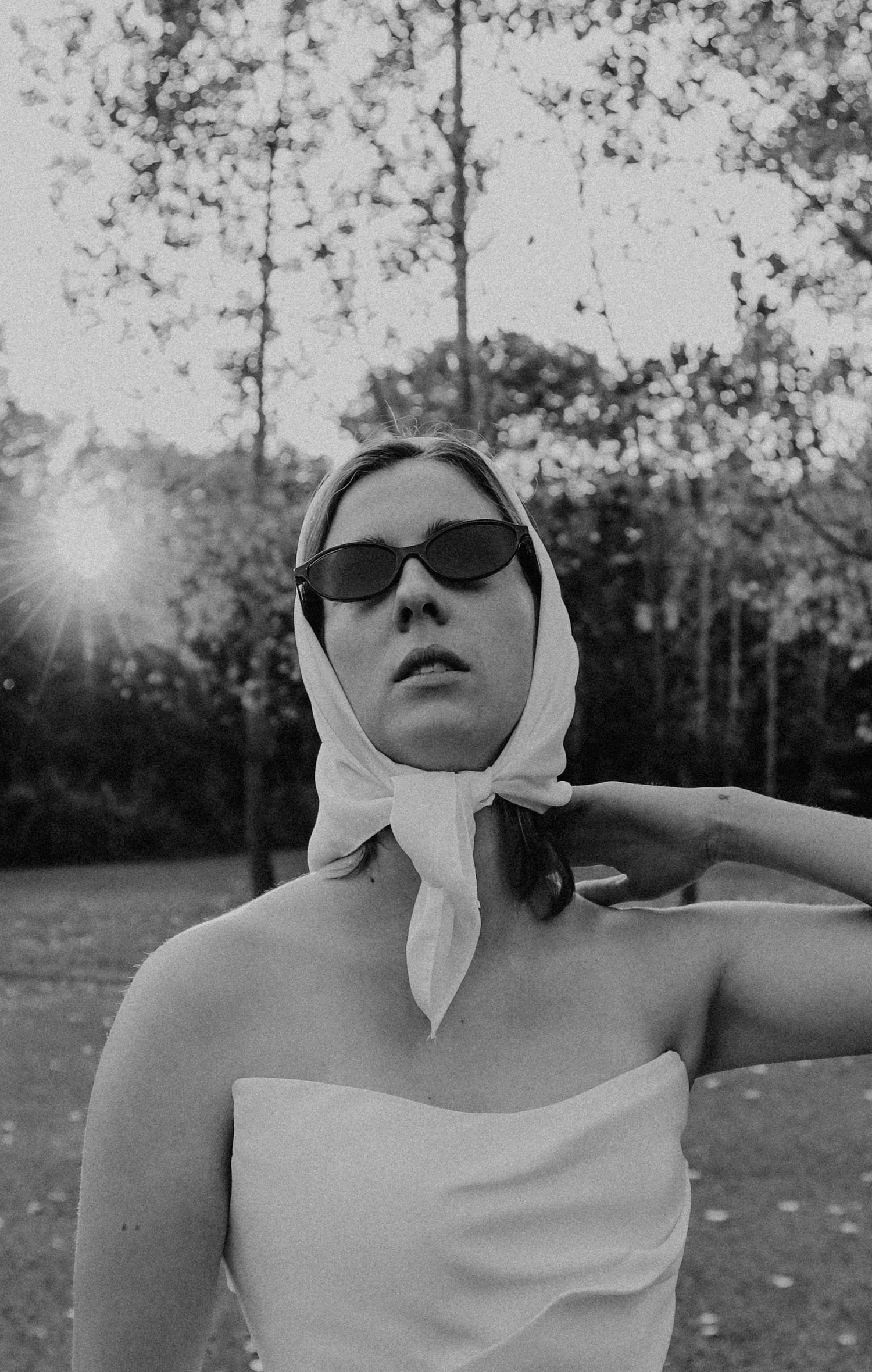 Black and white portrait of bride in strapless gown wearing sunglasses and white head scarf outdoors.