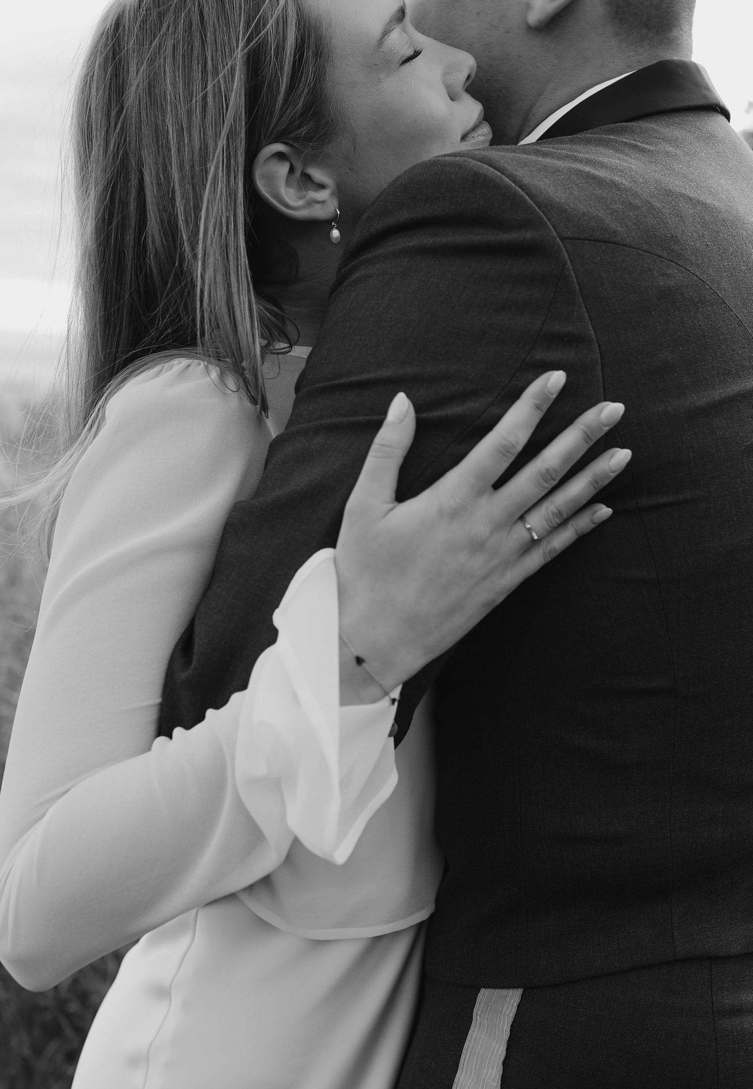 Black and white photo of bride and groom embracing, showing engagement ring on brides hand.