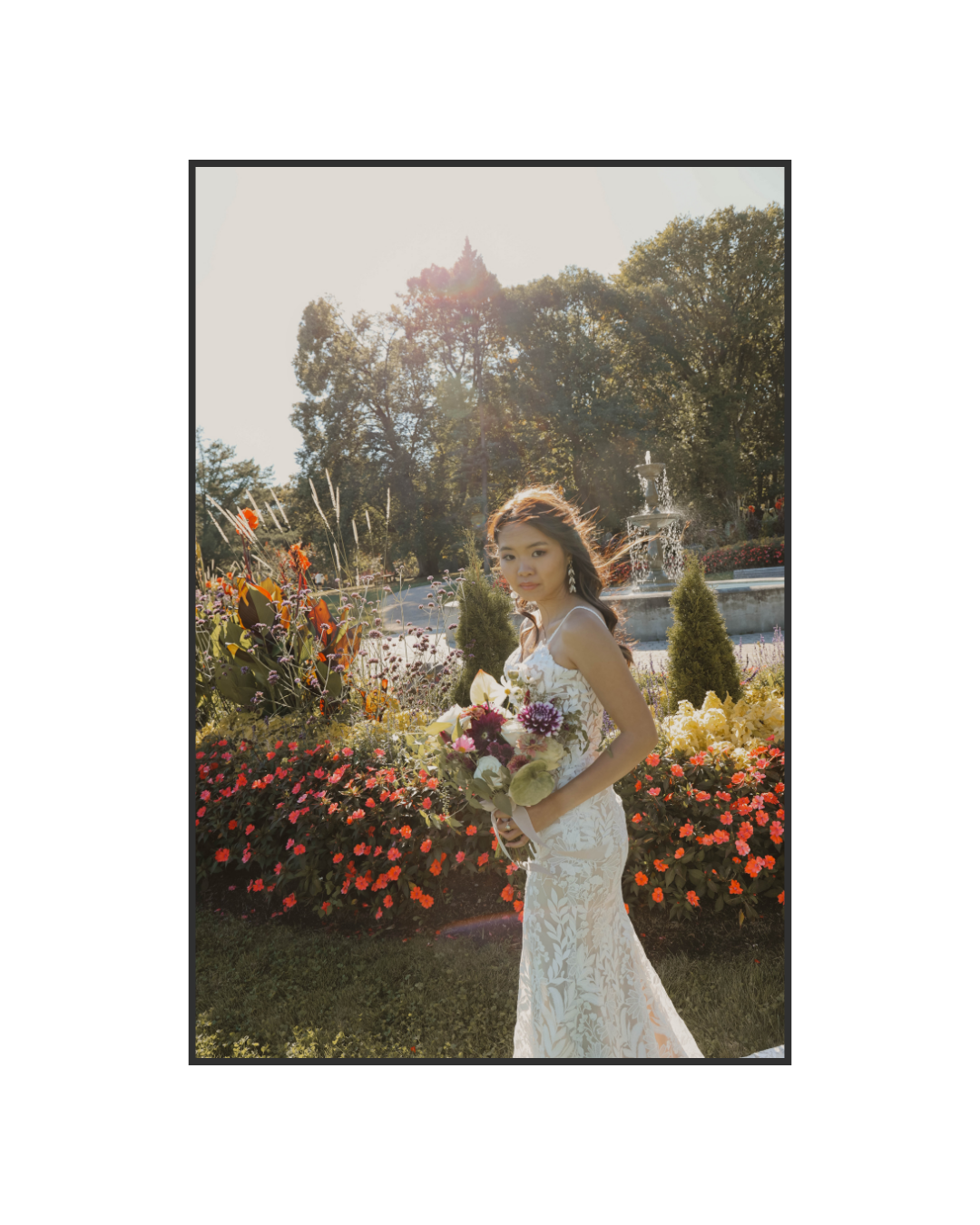 Bride in lace gown holding colorful bouquet standing in a sunlit garden with flowers.