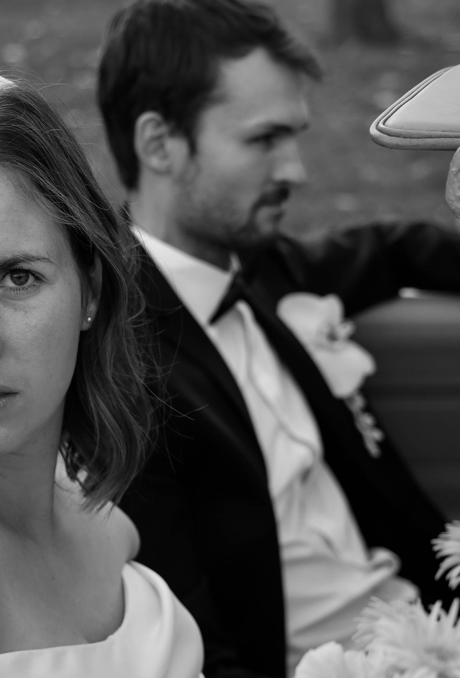 Black and white close-up of bride and groom sitting in a vintage convertible on their wedding day.