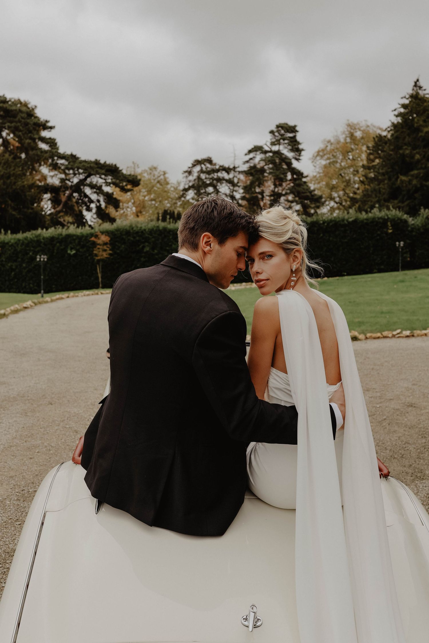 Romantic bride and groom sitting closely together on a vintage white convertible car at their wedding.