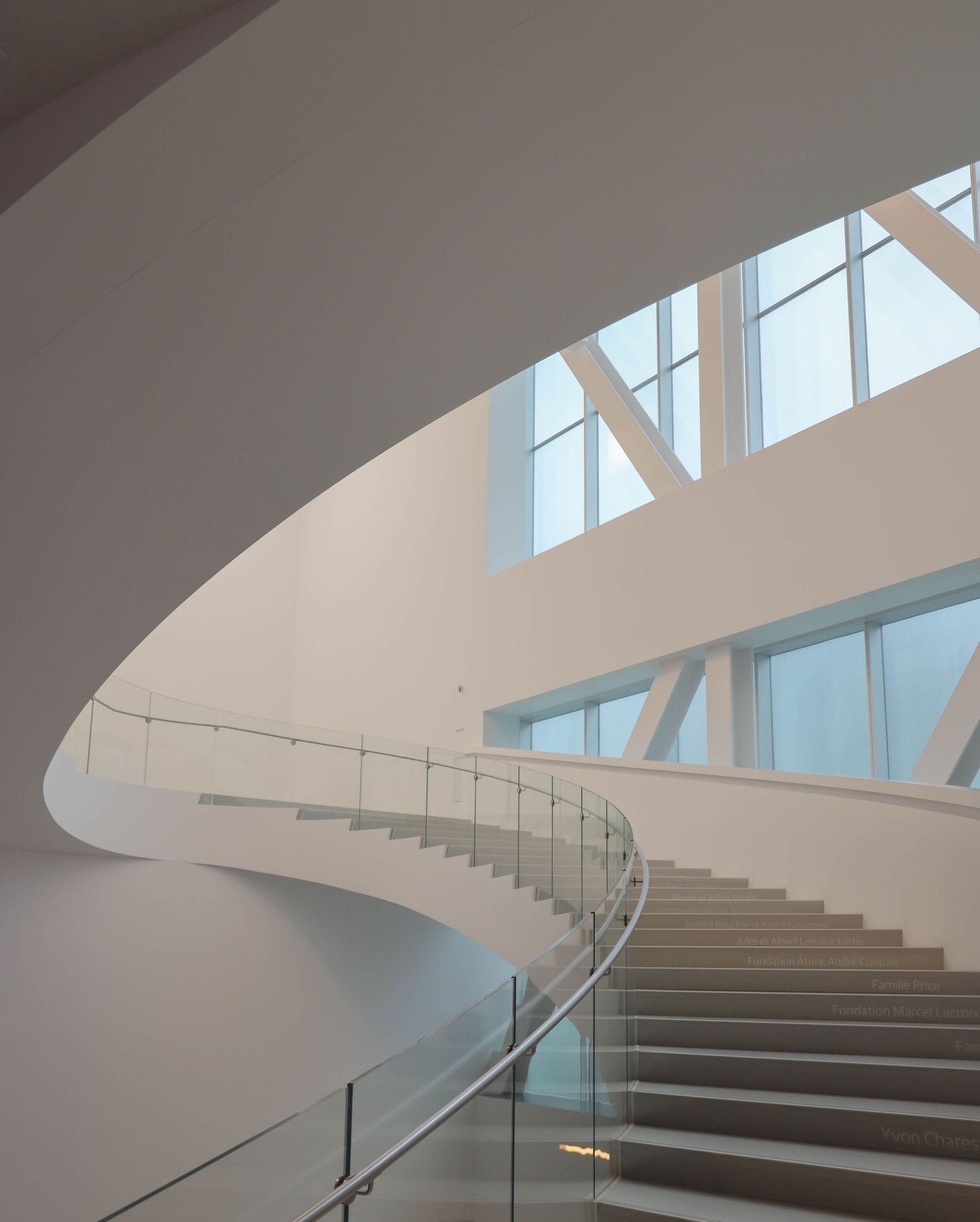 Elegant curved white spiral staircase with glass railings in a modern architectural interior.