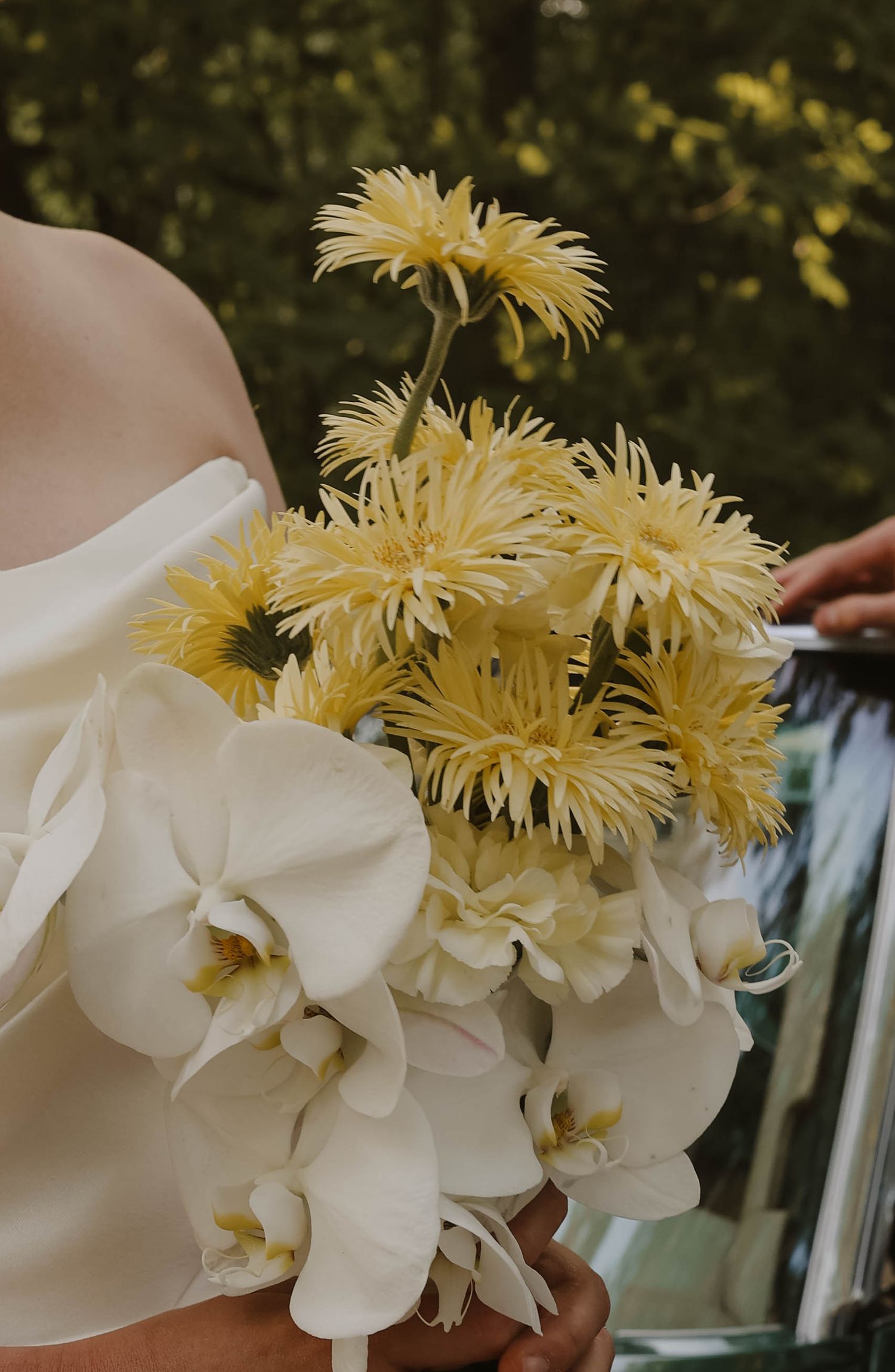 Bridal bouquet featuring yellow spider chrysanthemums and white orchids against a white gown.