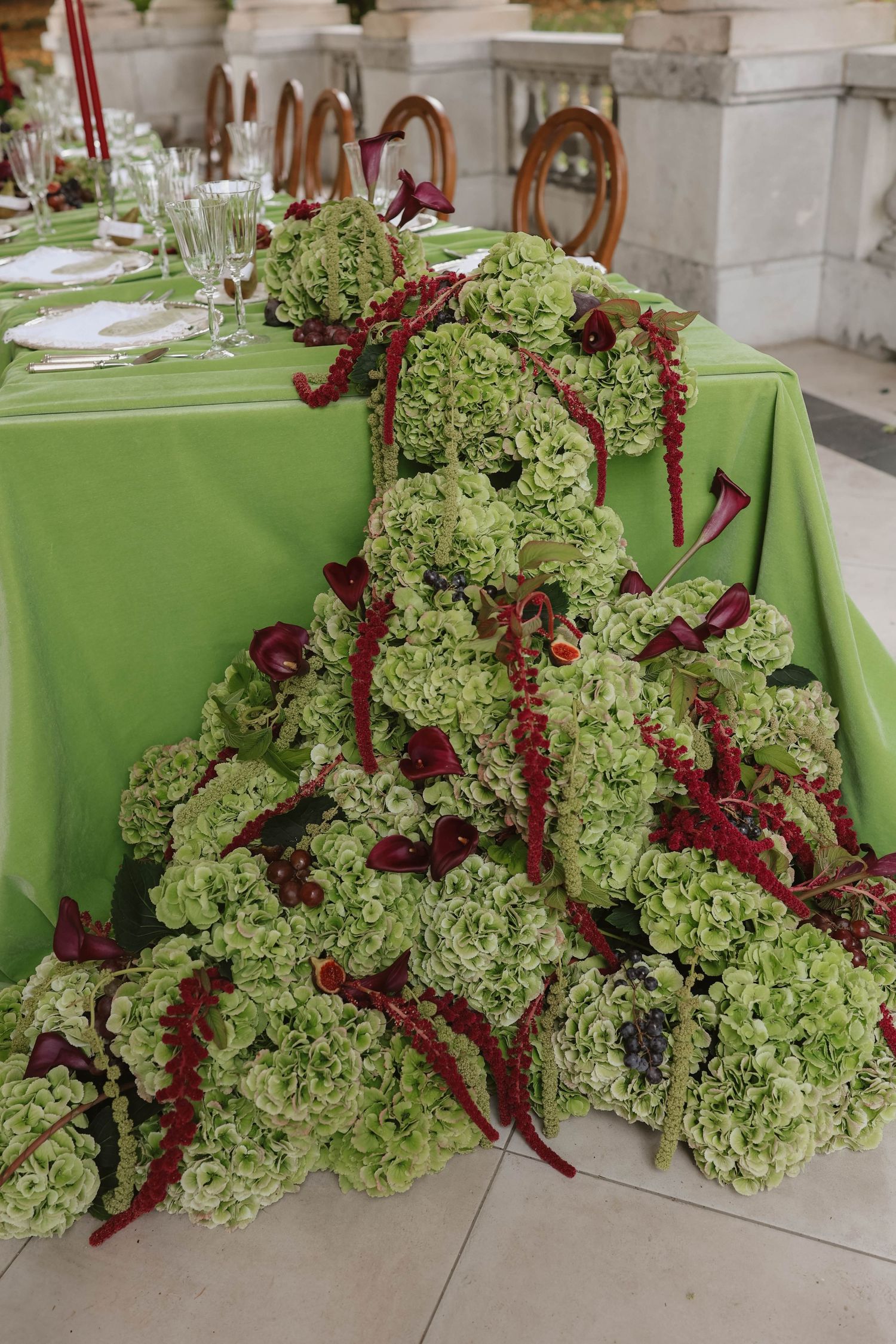 Stunning wedding table centerpiece with cascading green hydrangeas and deep red amaranthus on a green tablecloth.