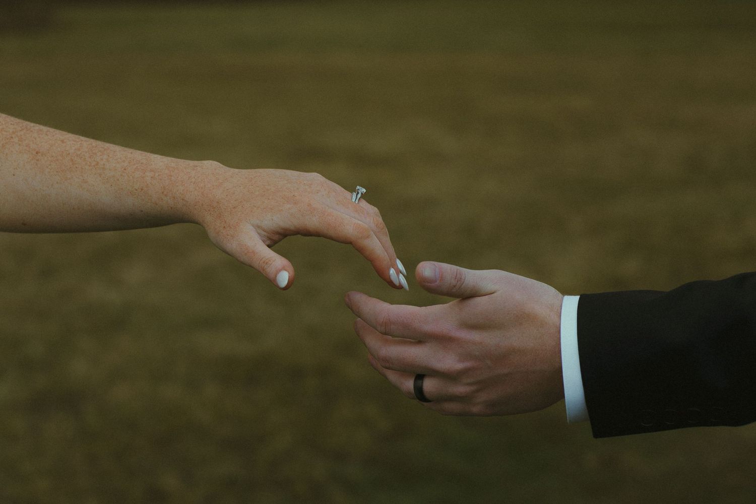 Close-up shot of hands exchanging wedding rings during an outdoor ceremony with a blurred natural background.