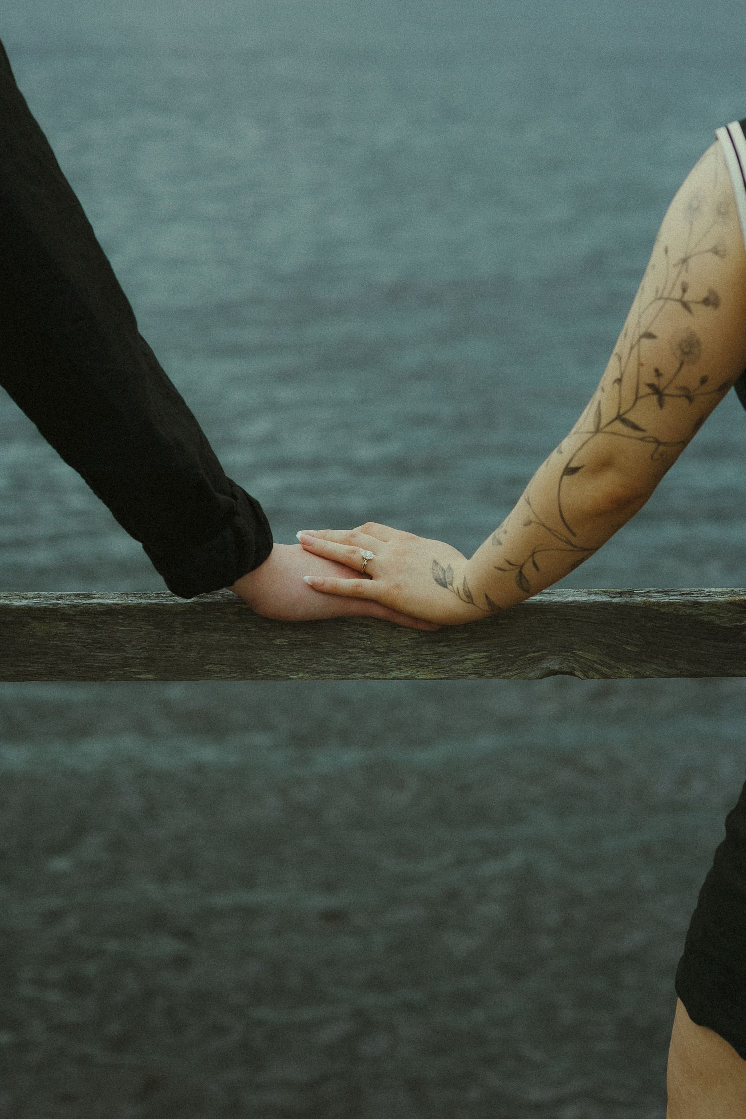 Two hands with tattoos reaching towards each other against a dark teal water background.