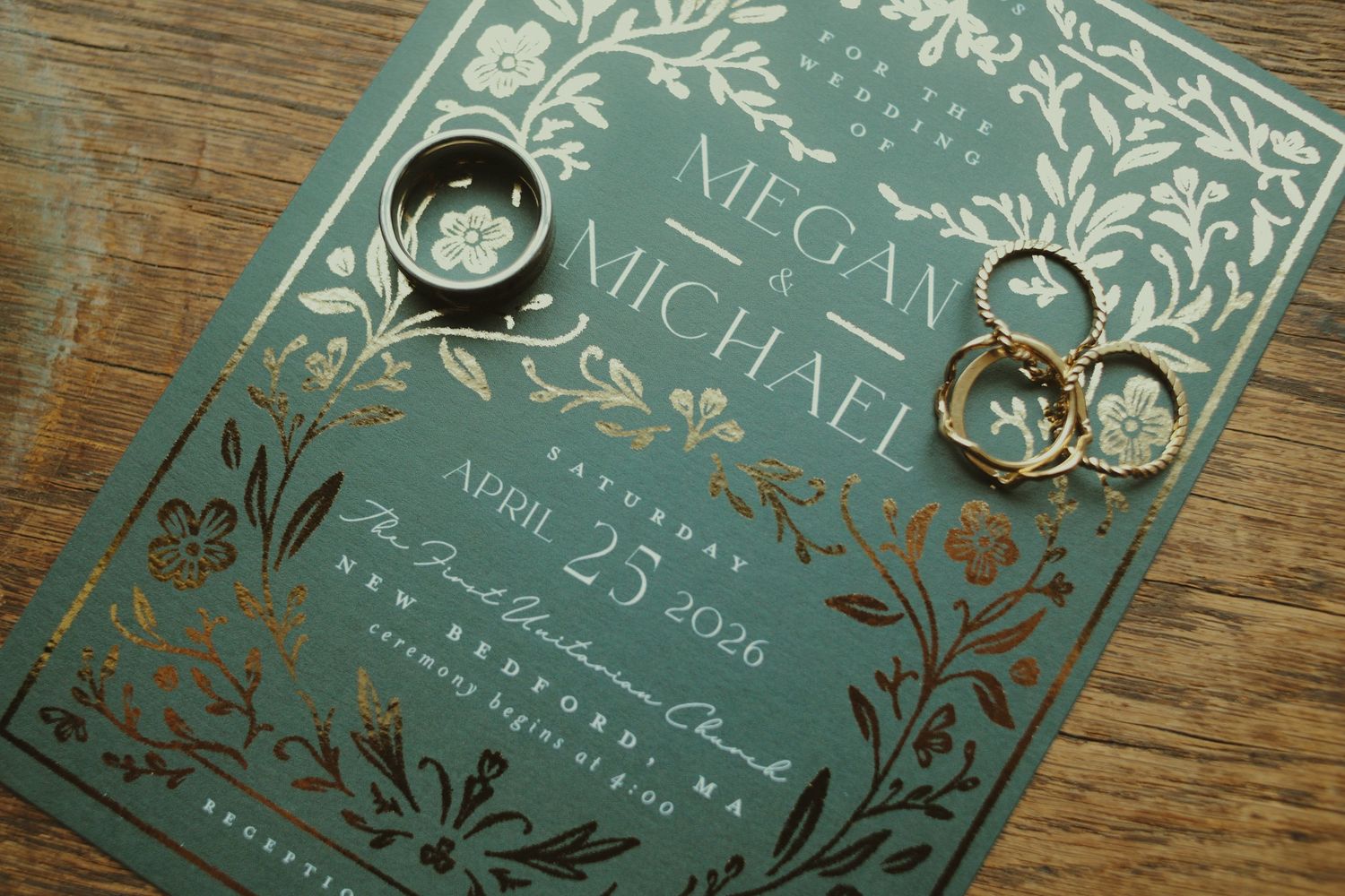 Elegant green and gold wedding invitation for Megan and Michael with floral details, accompanied by gold wedding rings.