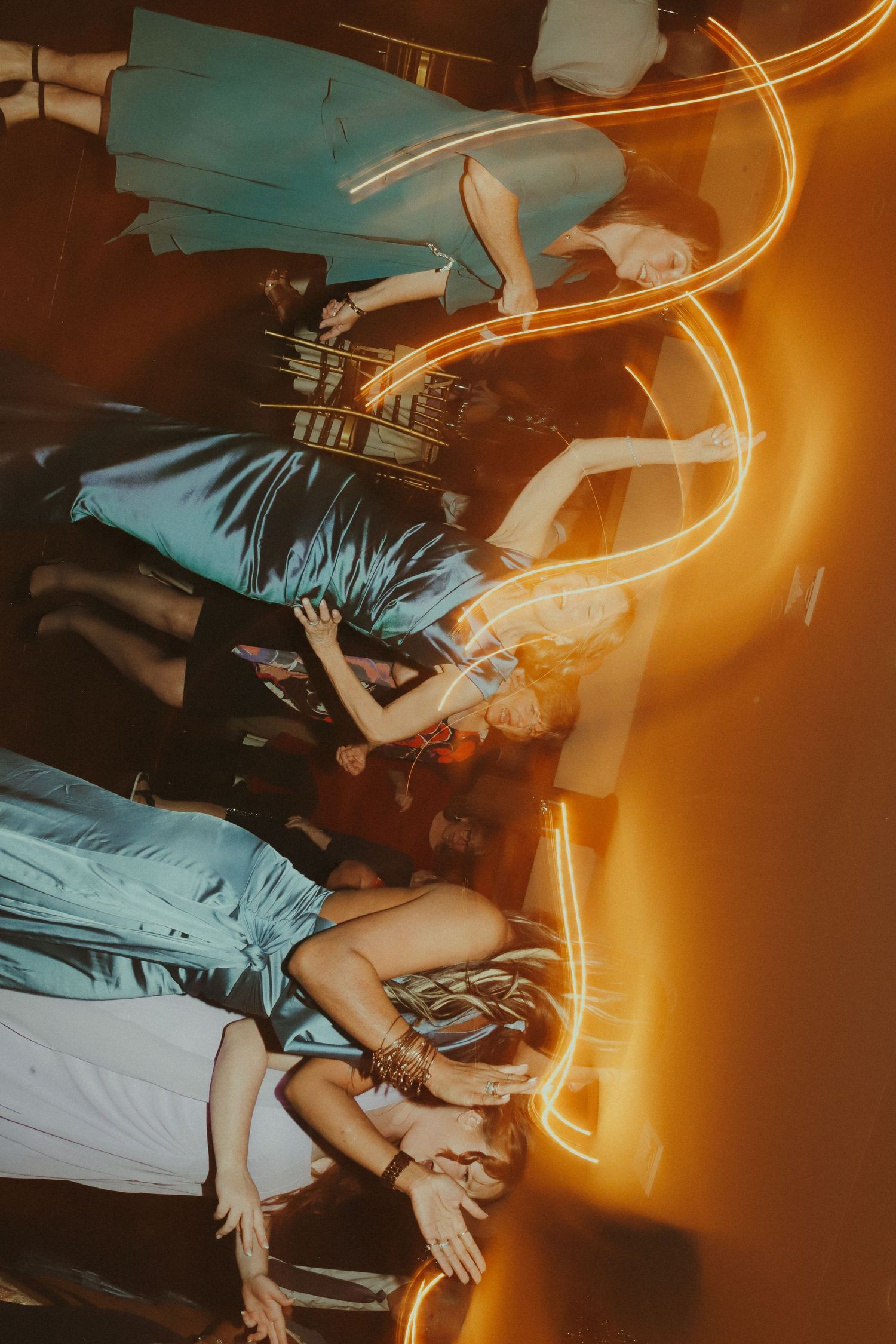 People dancing at a nightclub with vibrant orange light trails and motion blur creating an energetic atmosphere.