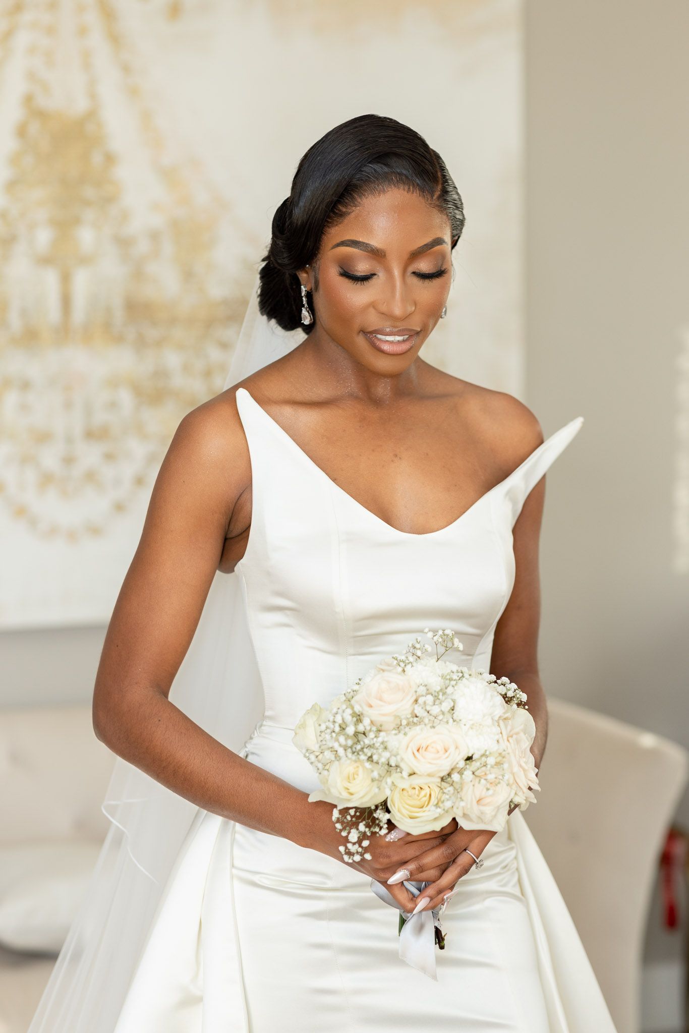 Bride in a classic white gown smiles while holding a beautiful bouquet of white roses and baby's breath.