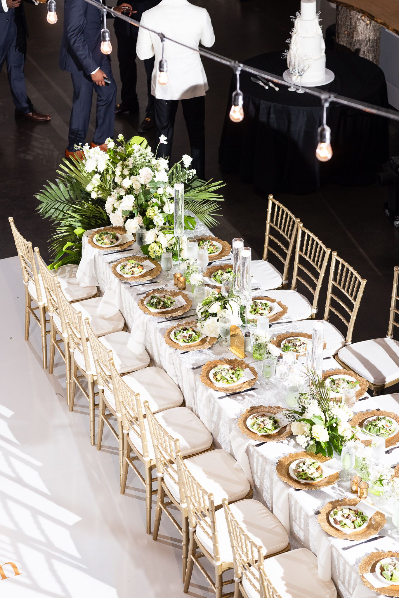 Long banquet table set with gold chairs and white linens at a formal wedding reception.
