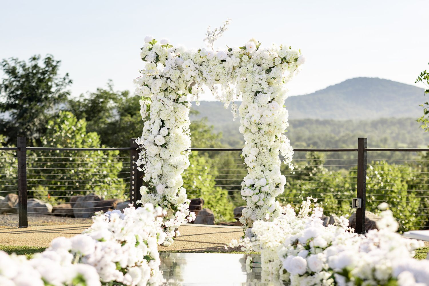 Luxurious white floral archway set against mountain landscape for outdoor ceremony.