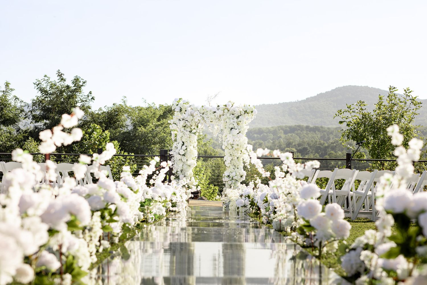 Elegant outdoor wedding reception setup with white floral arrangements and rustic wooden tables against a mountain backdrop.