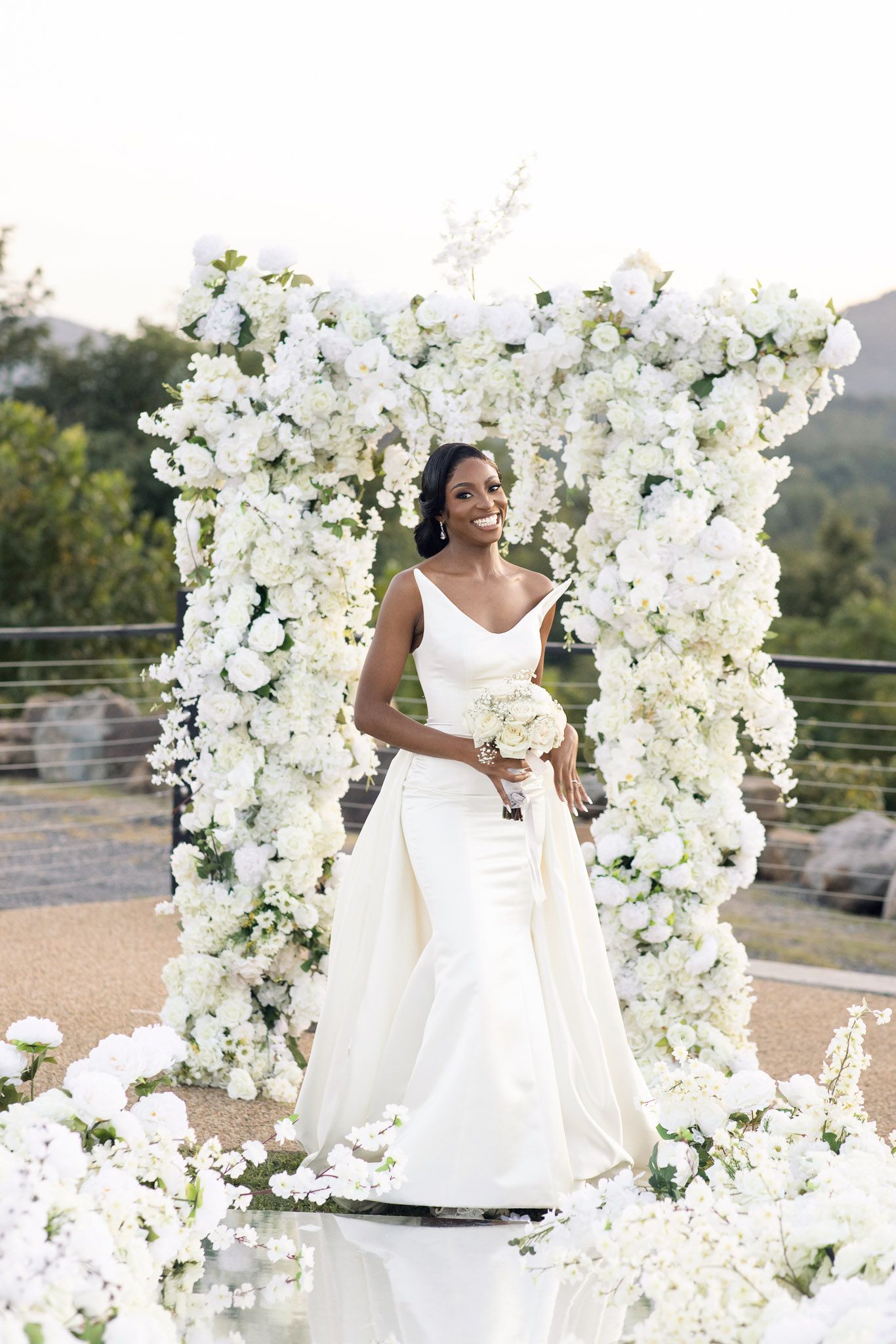 Beautiful white floral arch display at an outdoor wedding ceremony with mountain views.