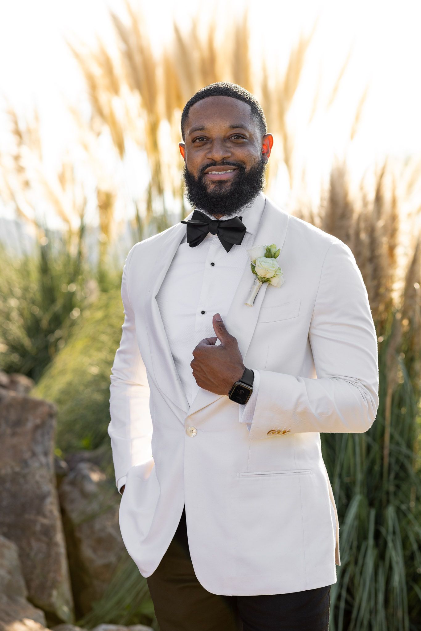 Classic white tuxedo with boutonniere photographed in natural outdoor setting.