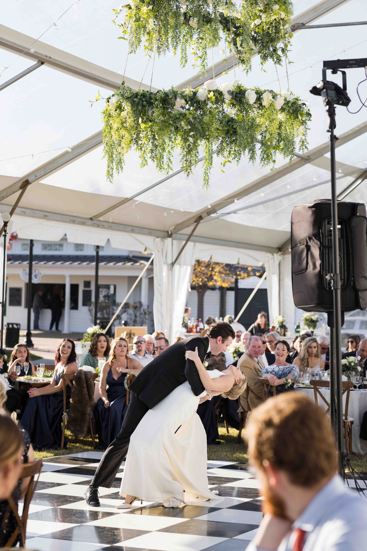 Wedding reception celebration under a white tent with guests dancing on a checkered dance floor.