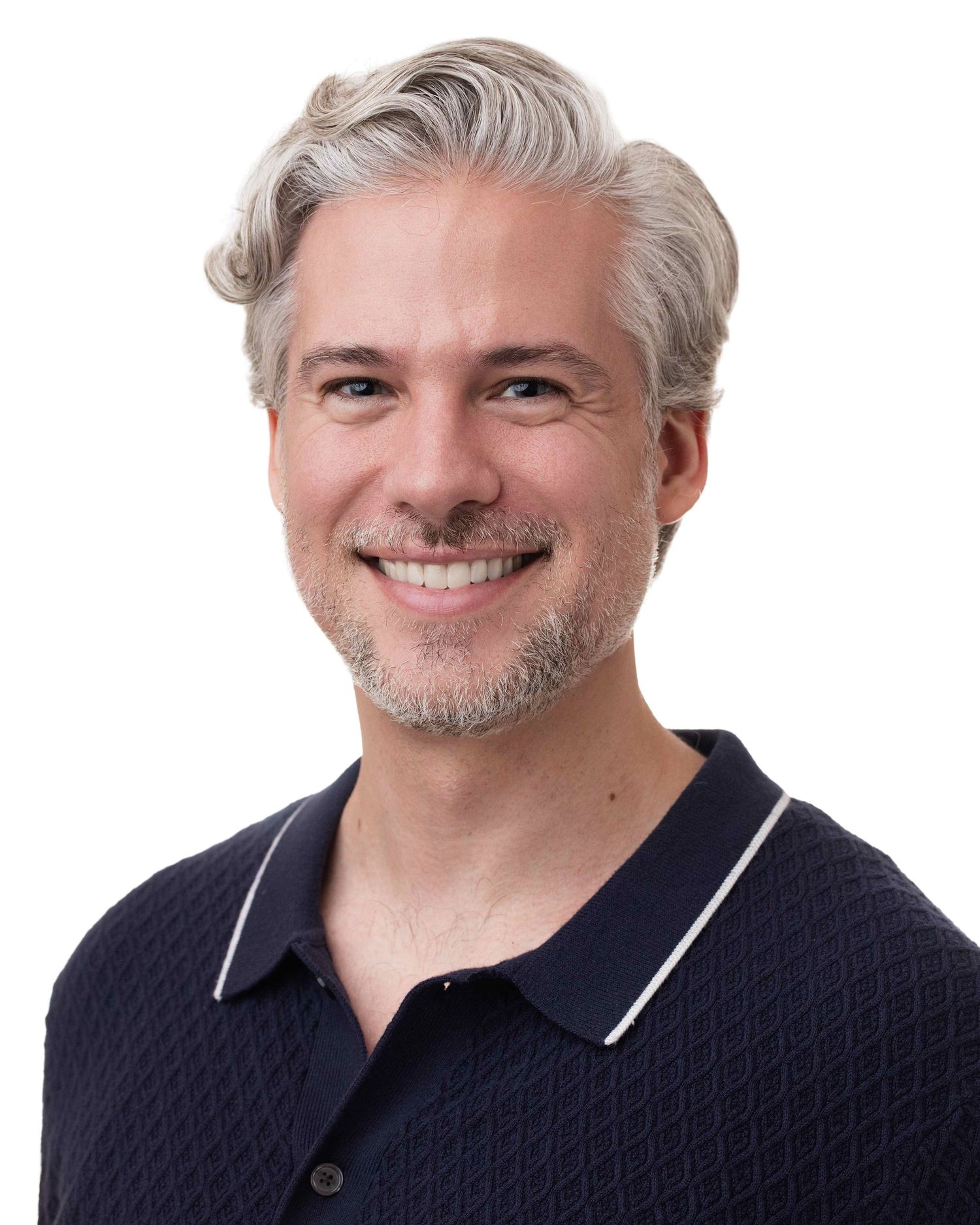 Smiling middle-aged man with silver hair and beard wearing a navy polo shirt against a white background.