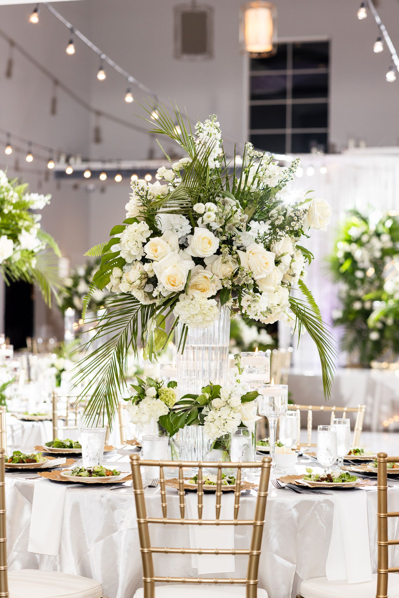 Modern wedding reception setup with tropical centerpieces and gold chiavari chairs.