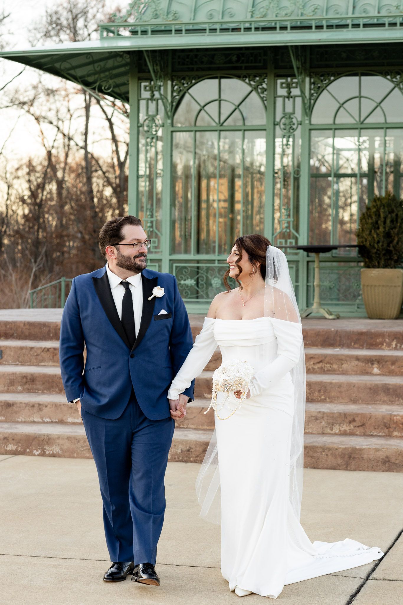 A couple shares a romantic moment in front of a glass greenhouse during their wedding photo session.