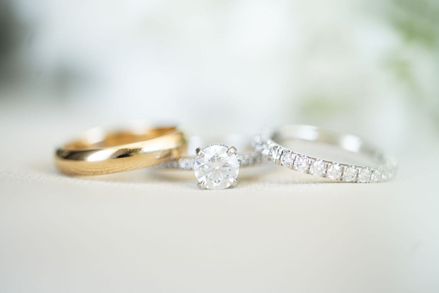 Three elegant rings displayed together: a gold band, a diamond solitaire engagement ring, and a diamond eternity band.