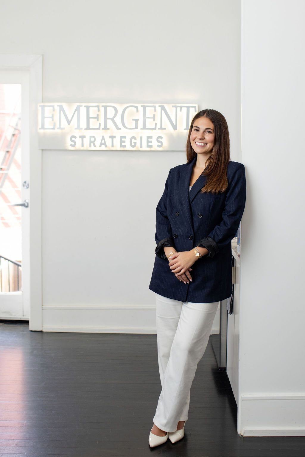 Professional woman in navy blazer and white pants smiling at Emergent Strategies office.