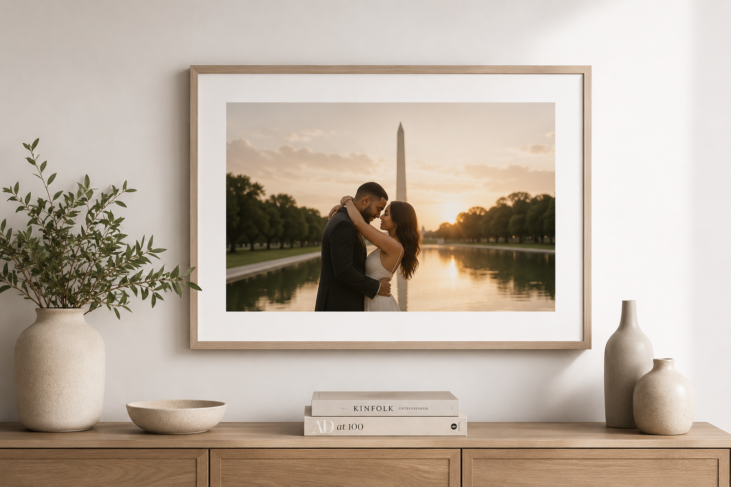 Framed wedding photo of couple kissing by Washington Monument reflecting pool at sunset, displayed above wooden dresser.