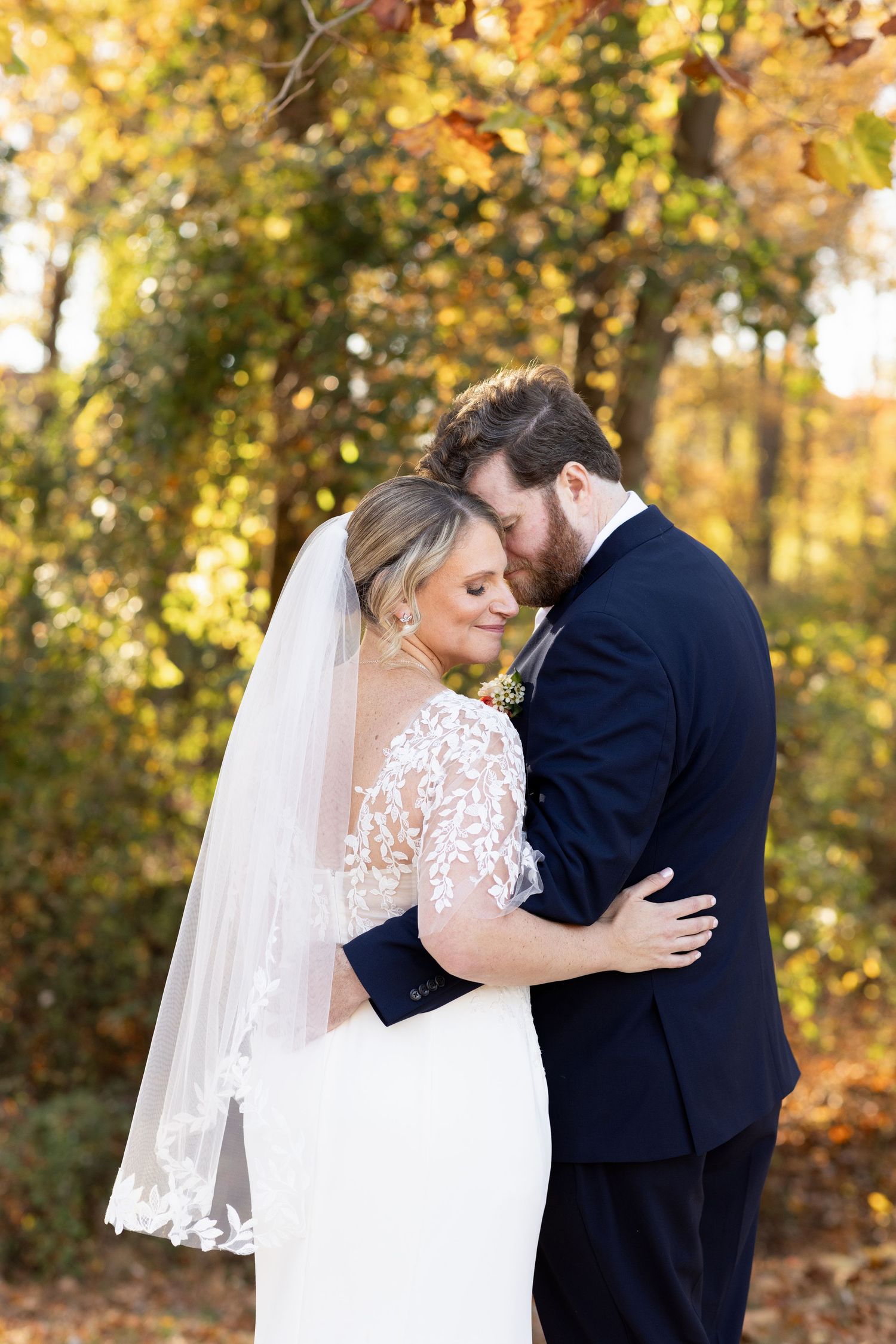 Bride and groom share intimate moment during fall wedding photoshoot with golden leaves behind.