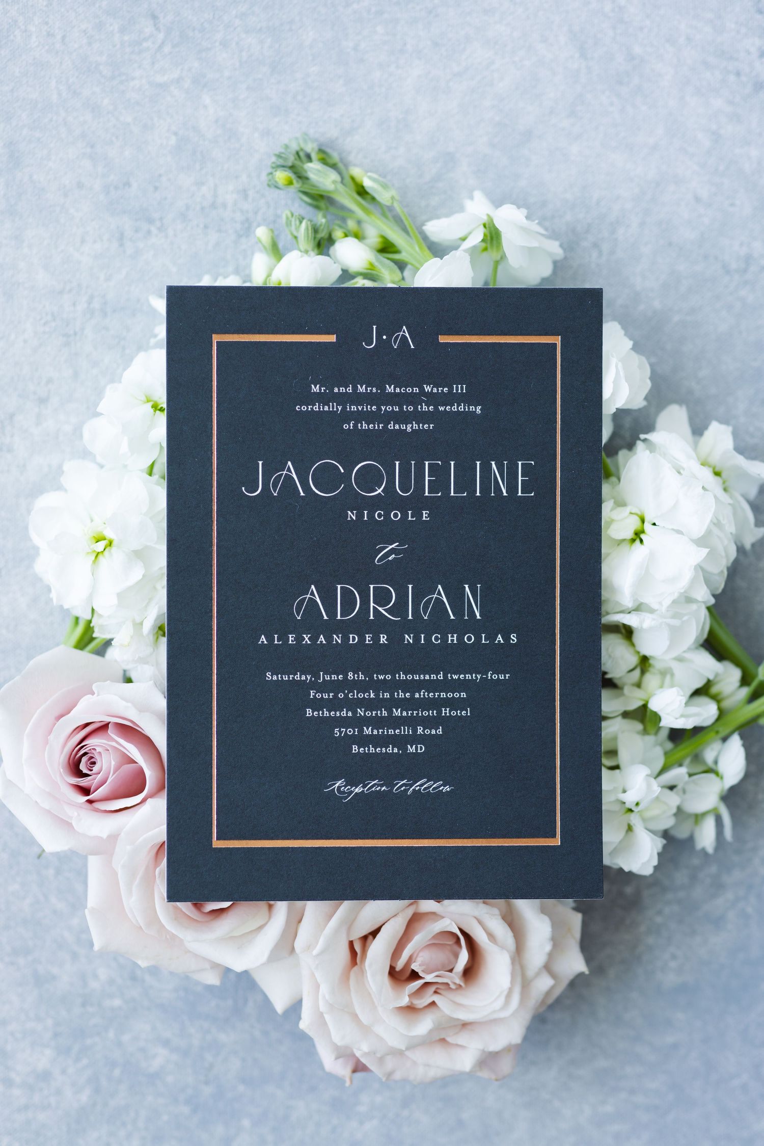 Navy blue wedding invitation with gold foil text surrounded by white flowers and pink roses.