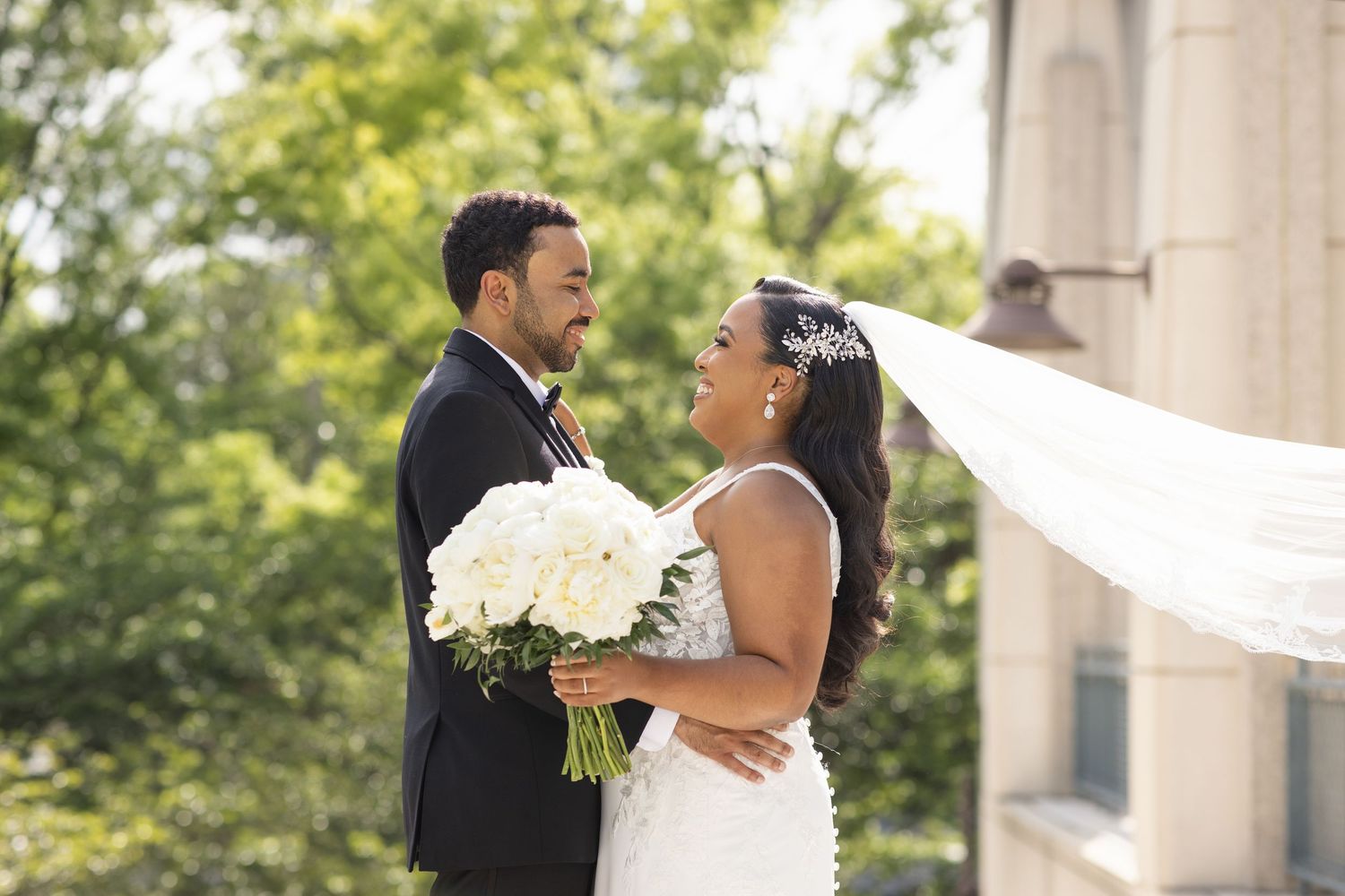 A happy couple embraces during their outdoor wedding ceremony with white floral decorations and natural greenery.