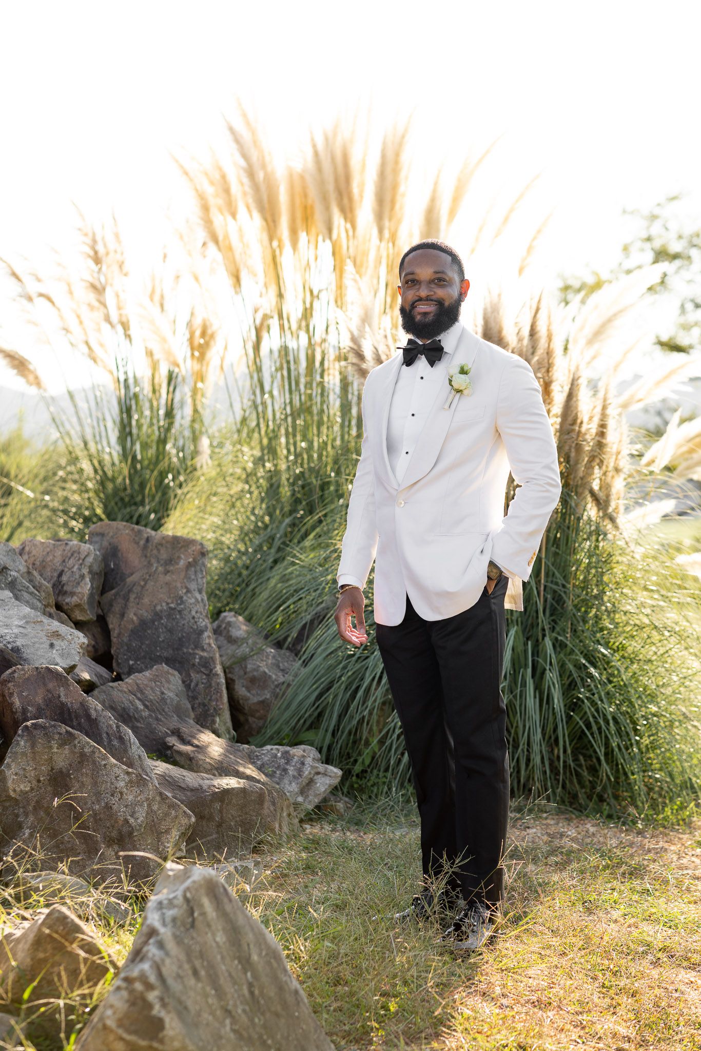 Classic white tuxedo jacket and black pants against outdoor natural landscape.