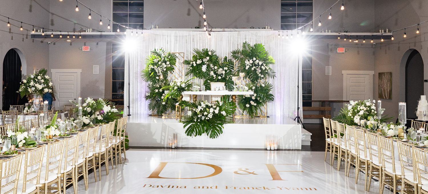 Panoramic view of an elegant white wedding reception hall with string lights and gold chairs.