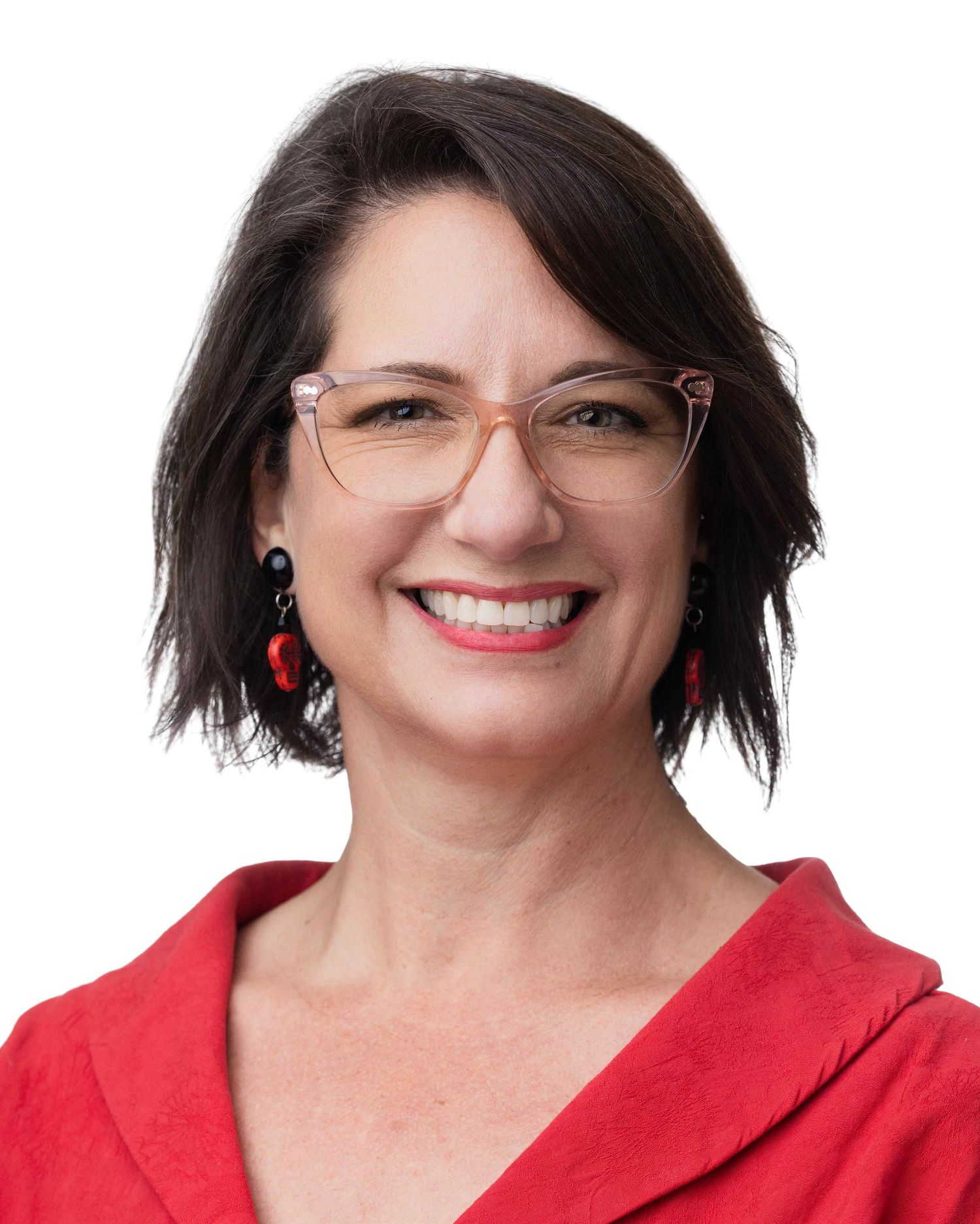 Smiling woman with short dark hair, pink glasses, and red earrings wearing a red top against a white background.