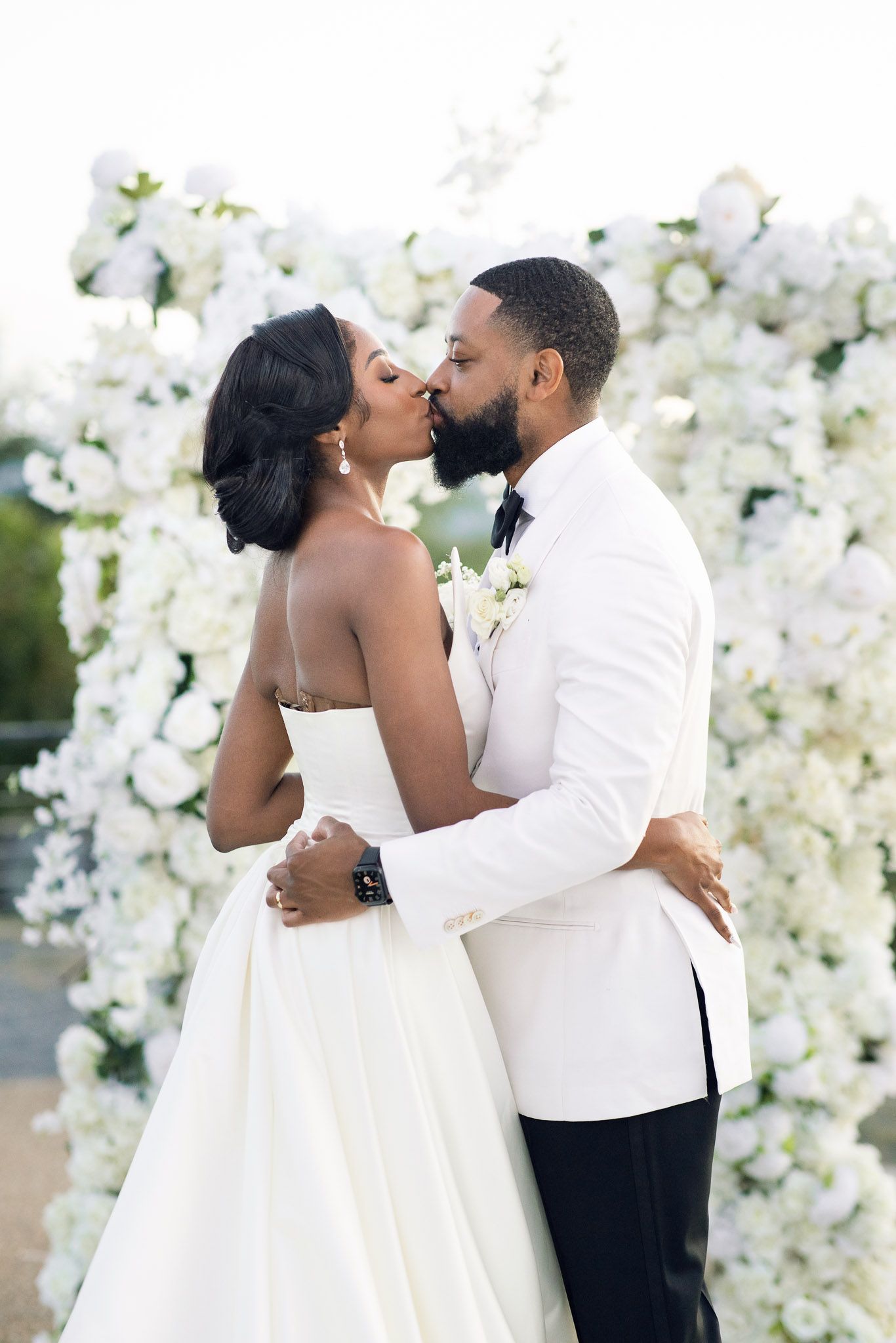 A romantic wedding ceremony moment under a white floral arch with lush decorative flowers.