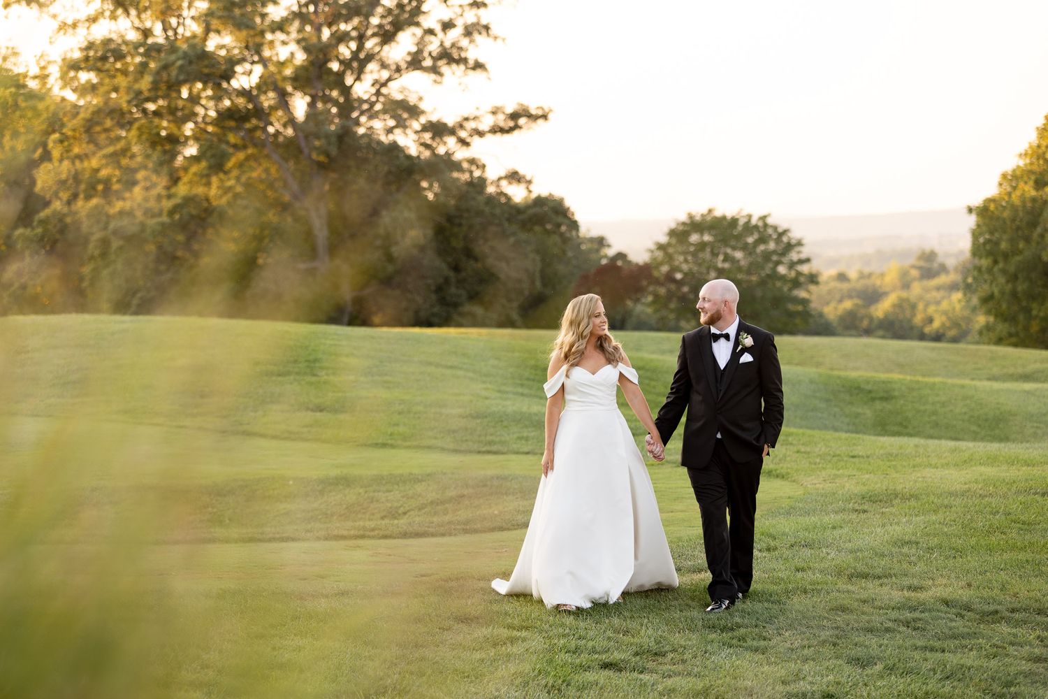 A couple walks together on a lush green hillside during golden hour at sunset.