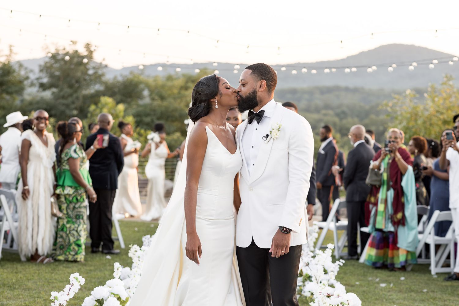 Outdoor wedding ceremony setup with string lights and mountain scenery in the background.
