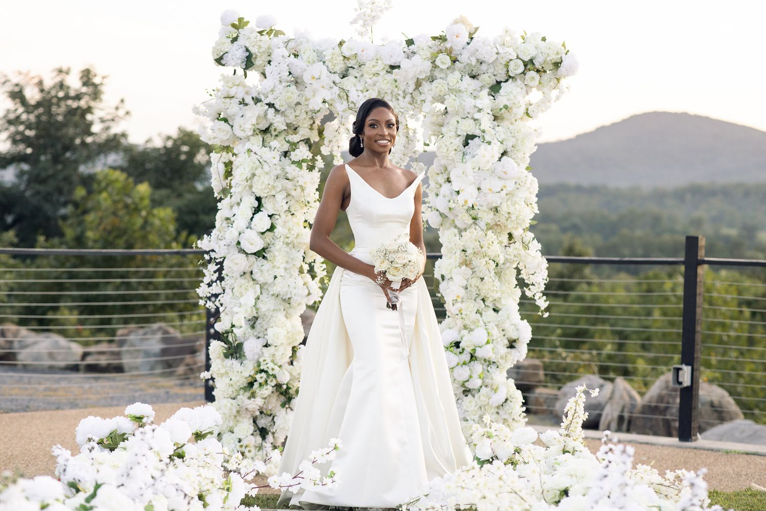 Luxurious white floral arch installation at a hilltop wedding ceremony.