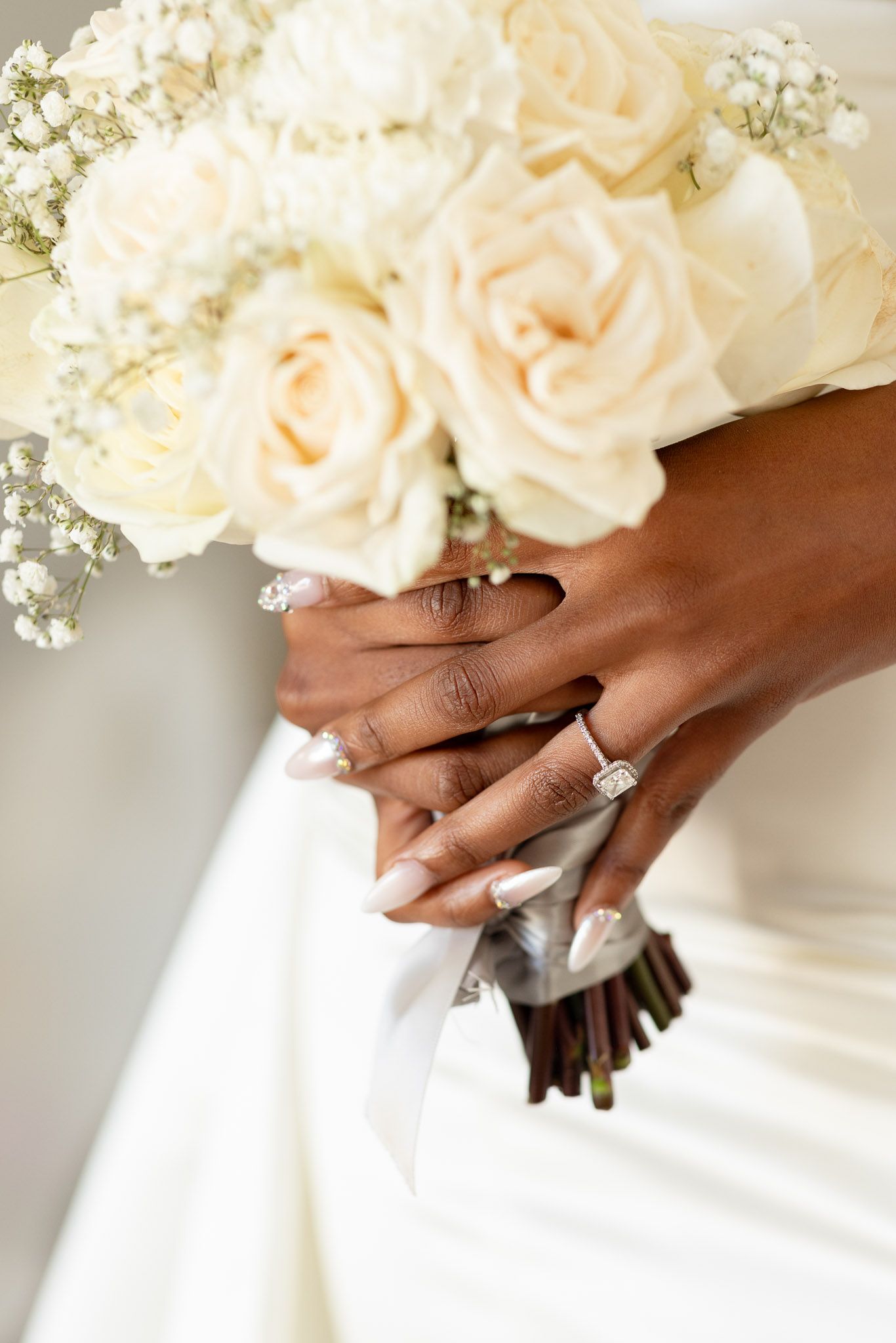 Detail shots of hands holding a white rose bouquet against a wedding dress.