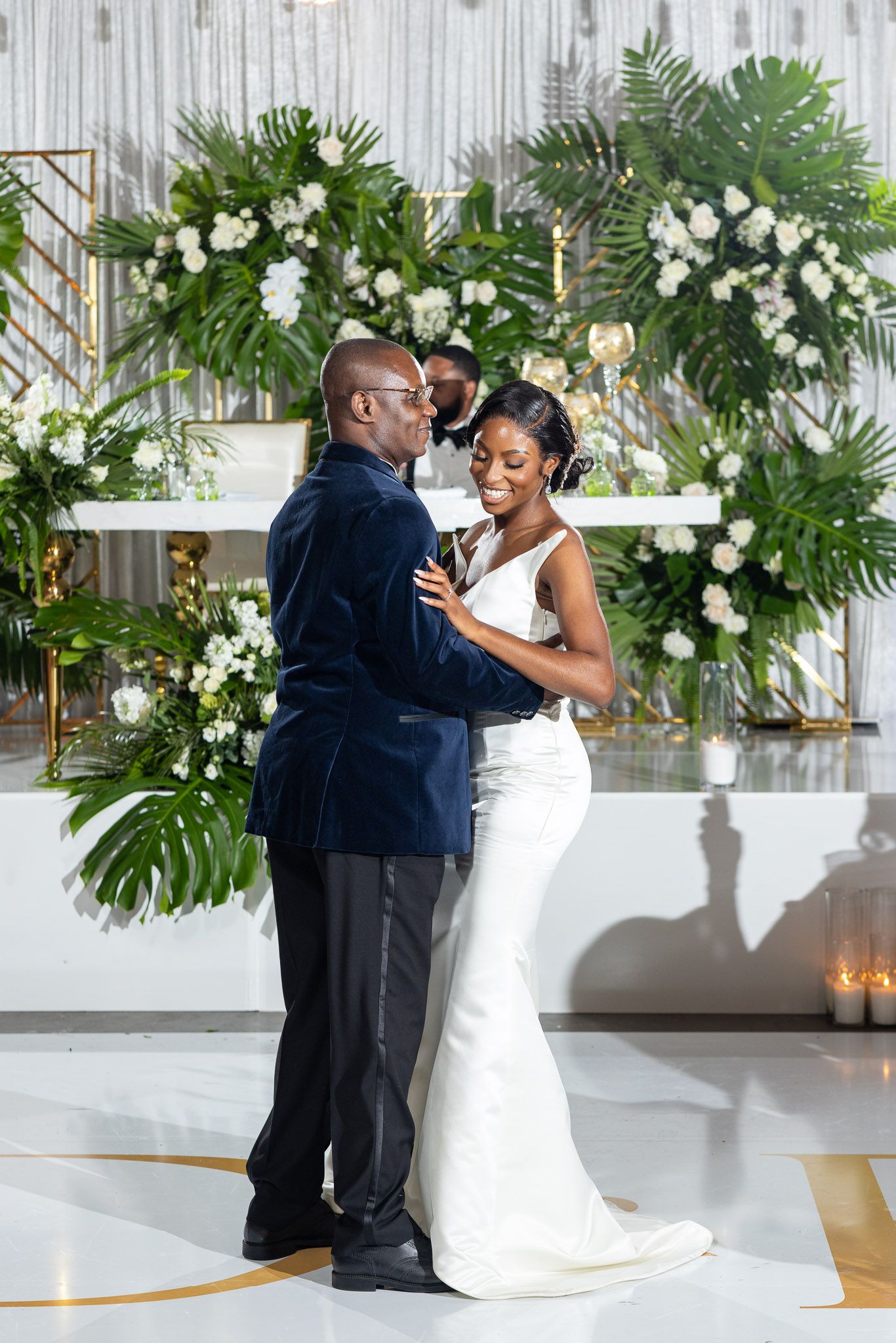 Newlyweds dancing together in an elegant venue decorated with white flowers and tropical leaves.
