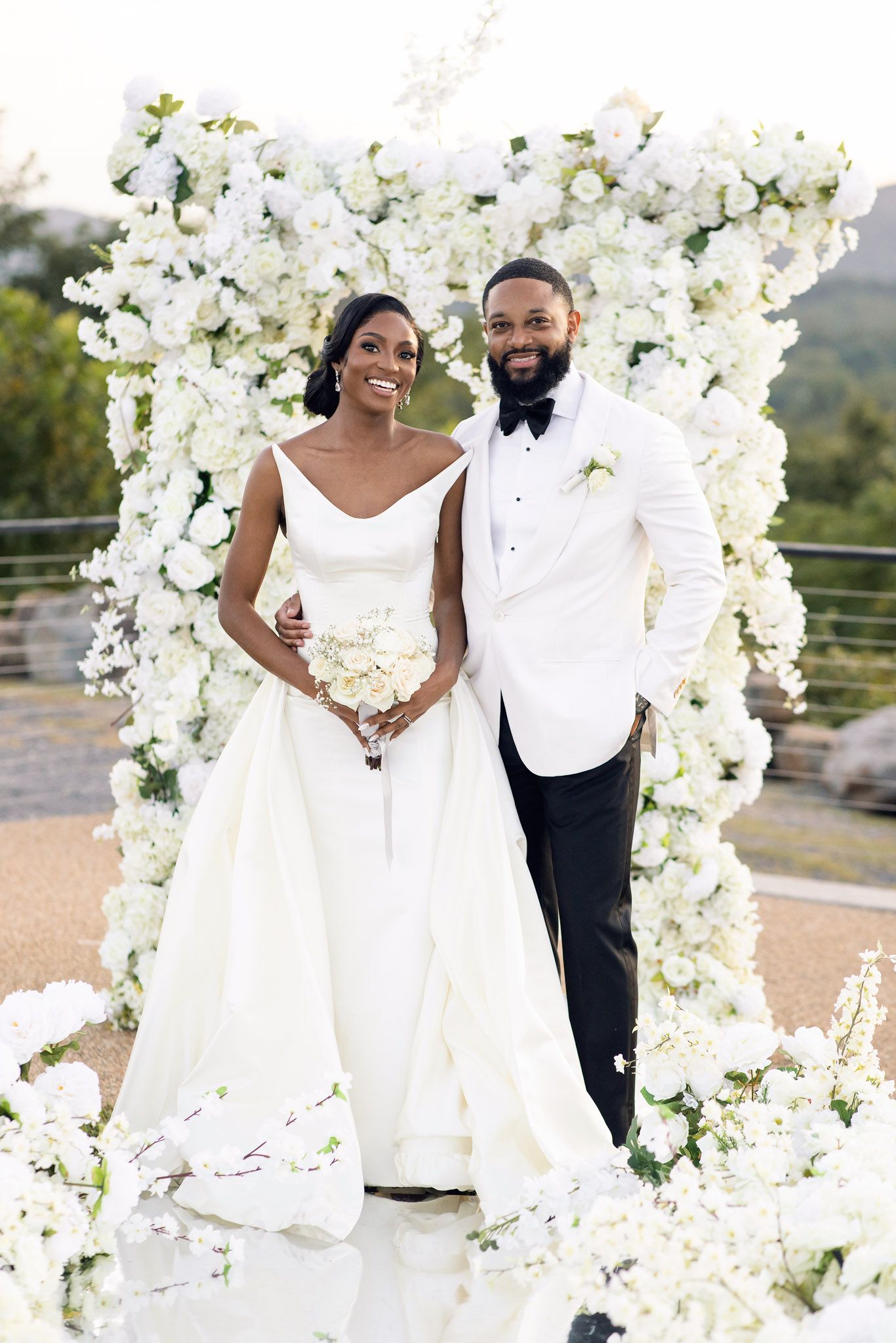 Elegant wedding portrait with couple standing before white flower arch.