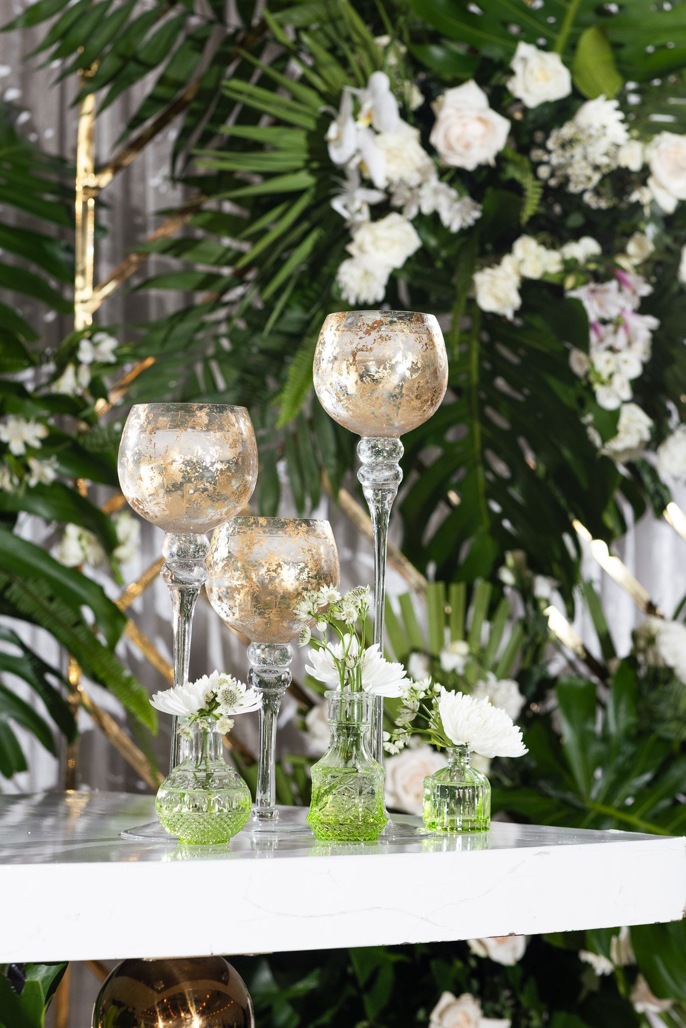 Elegant wedding table decor with gold mercury glass vases, white flowers and tropical greenery.